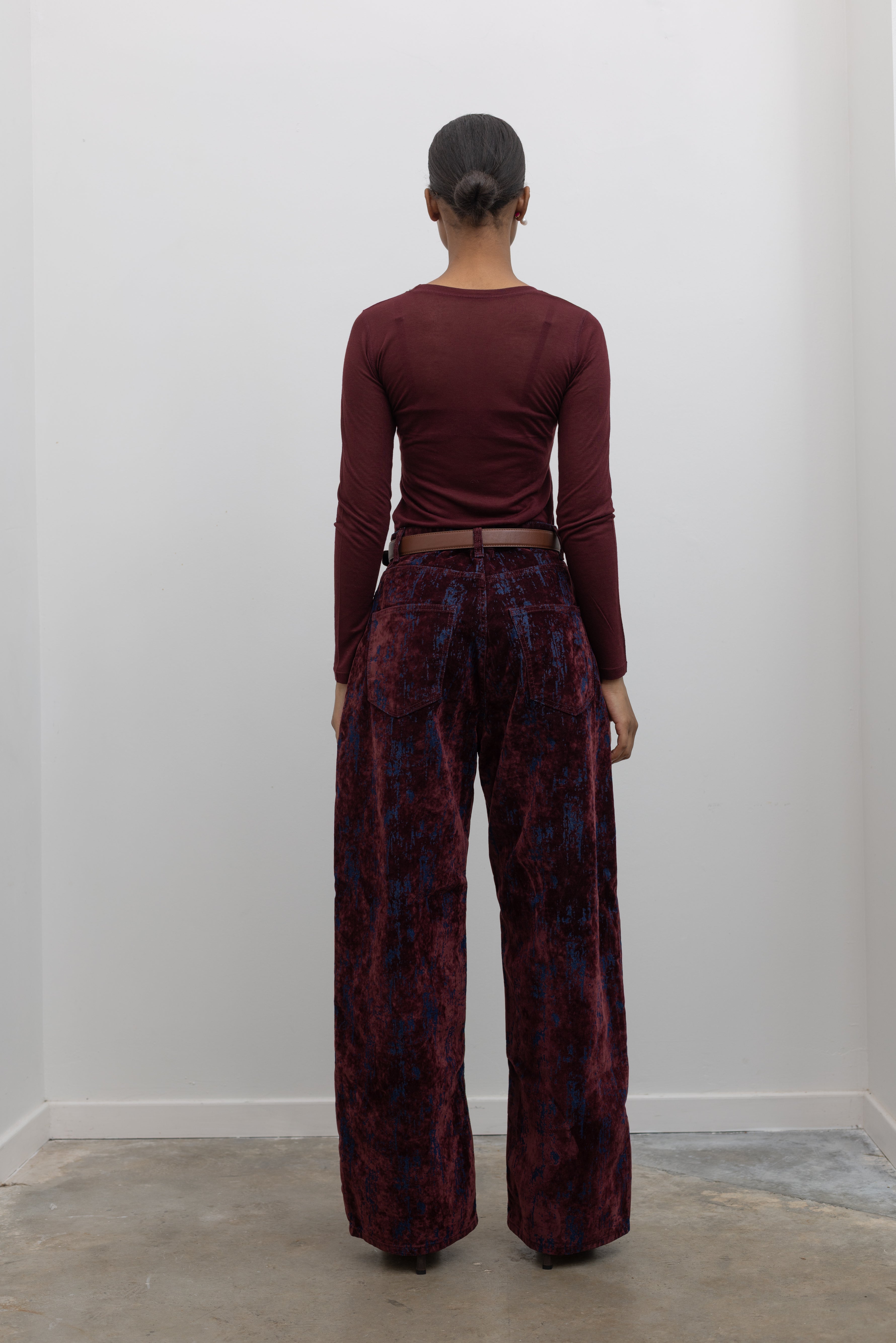 Full length back view of statement Paper Moon wide leg jeans in a luxurious burgundy distressed crackle velvet finish and a relaxed fit and a burgundy fitted knit long sleeve top at an Alas Eius store. 