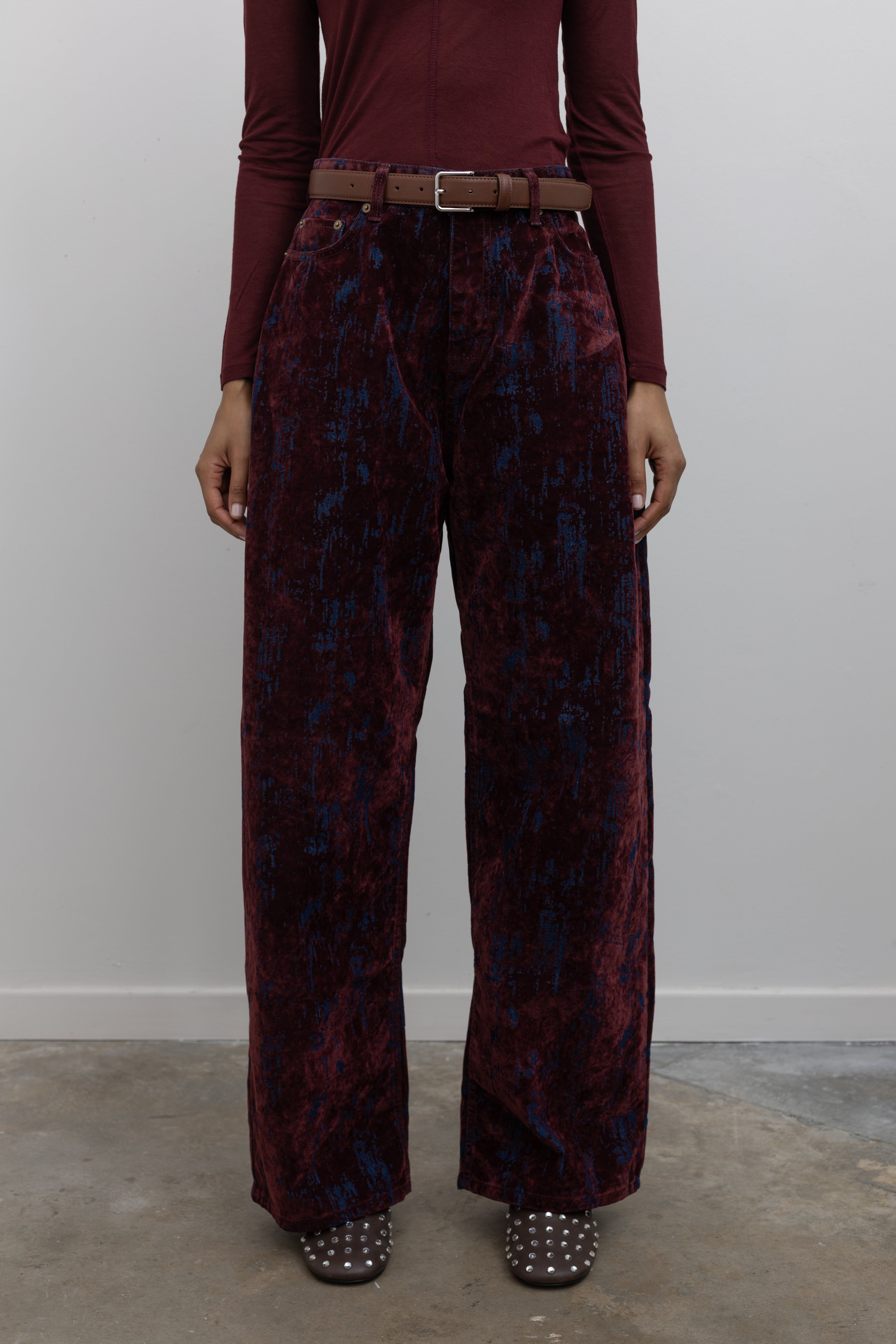 Close-up front view of statement Paper Moon wide leg jeans in a luxurious burgundy distressed crackle velvet finish and a relaxed fit at an Alas Eius store. 