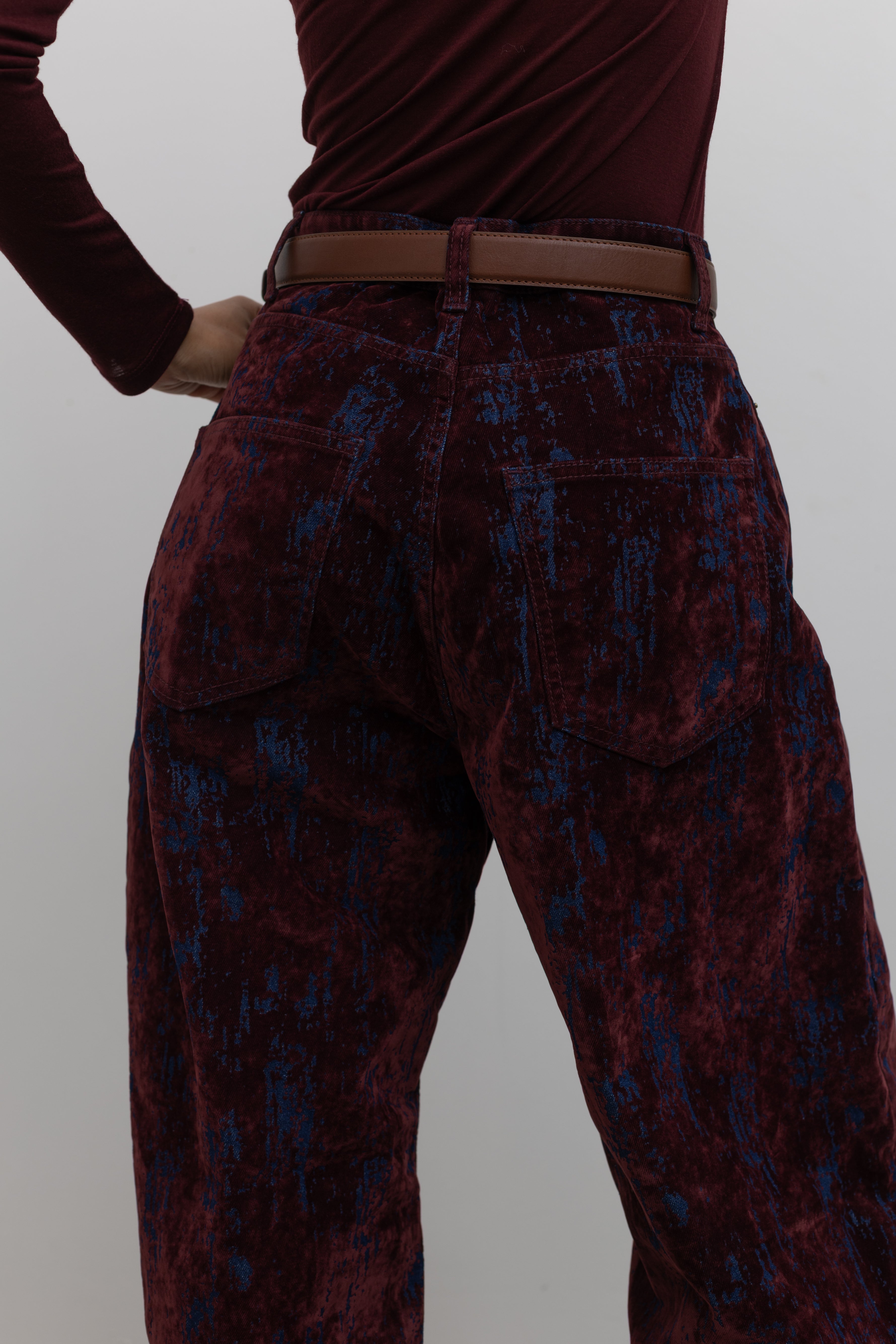 Close-up back view of statement Paper Moon wide leg jeans in a luxurious burgundy distressed crackle velvet finish and a relaxed fit at an Alas Eius store. 