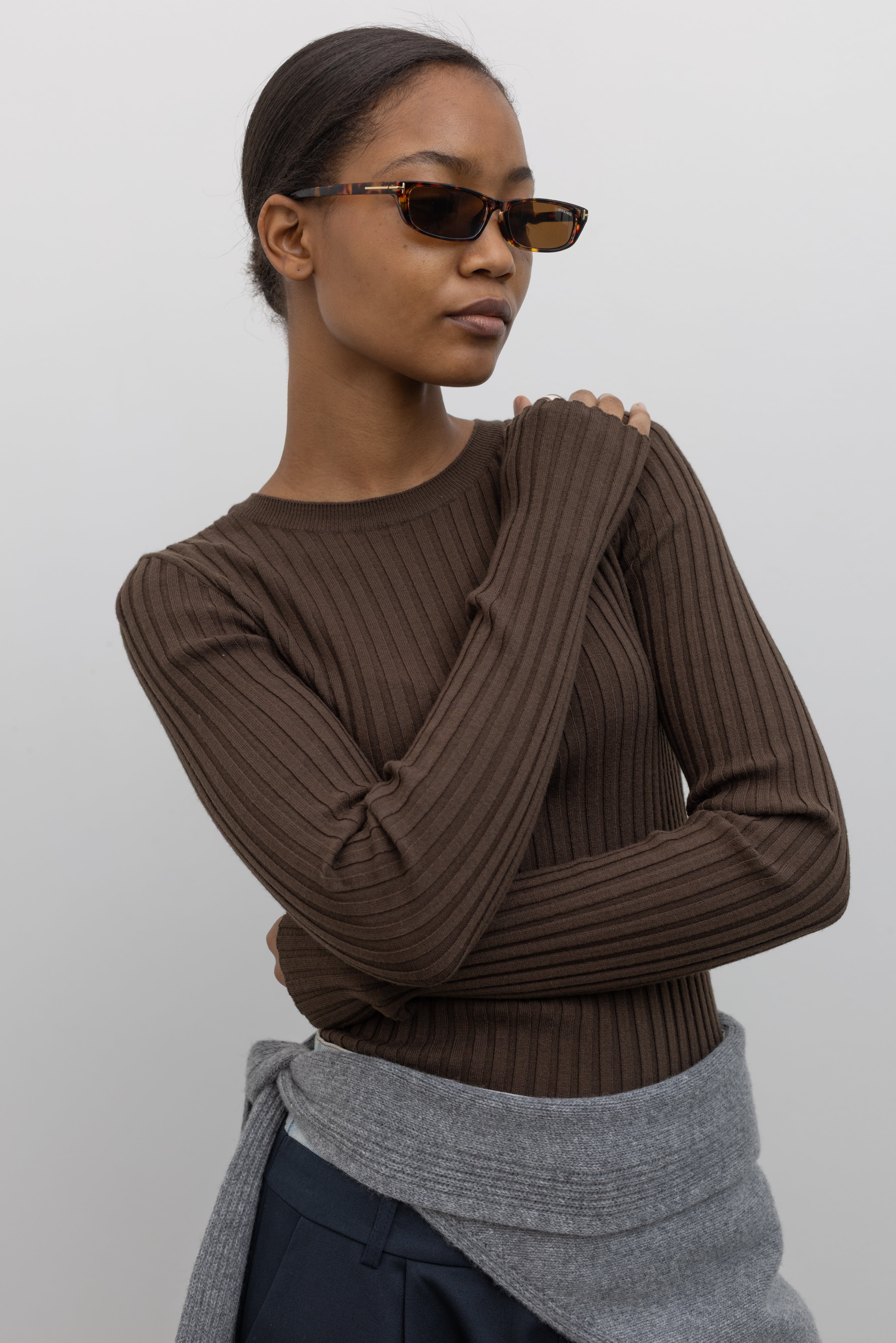 Close-up view of a woman wearing an elevated essential spring staple in a Paper Moon brand brown wool blend ribbed long sleeve fitted top with navy blue trousers and a gray bandana scarf around her waist at an Alas Eius 