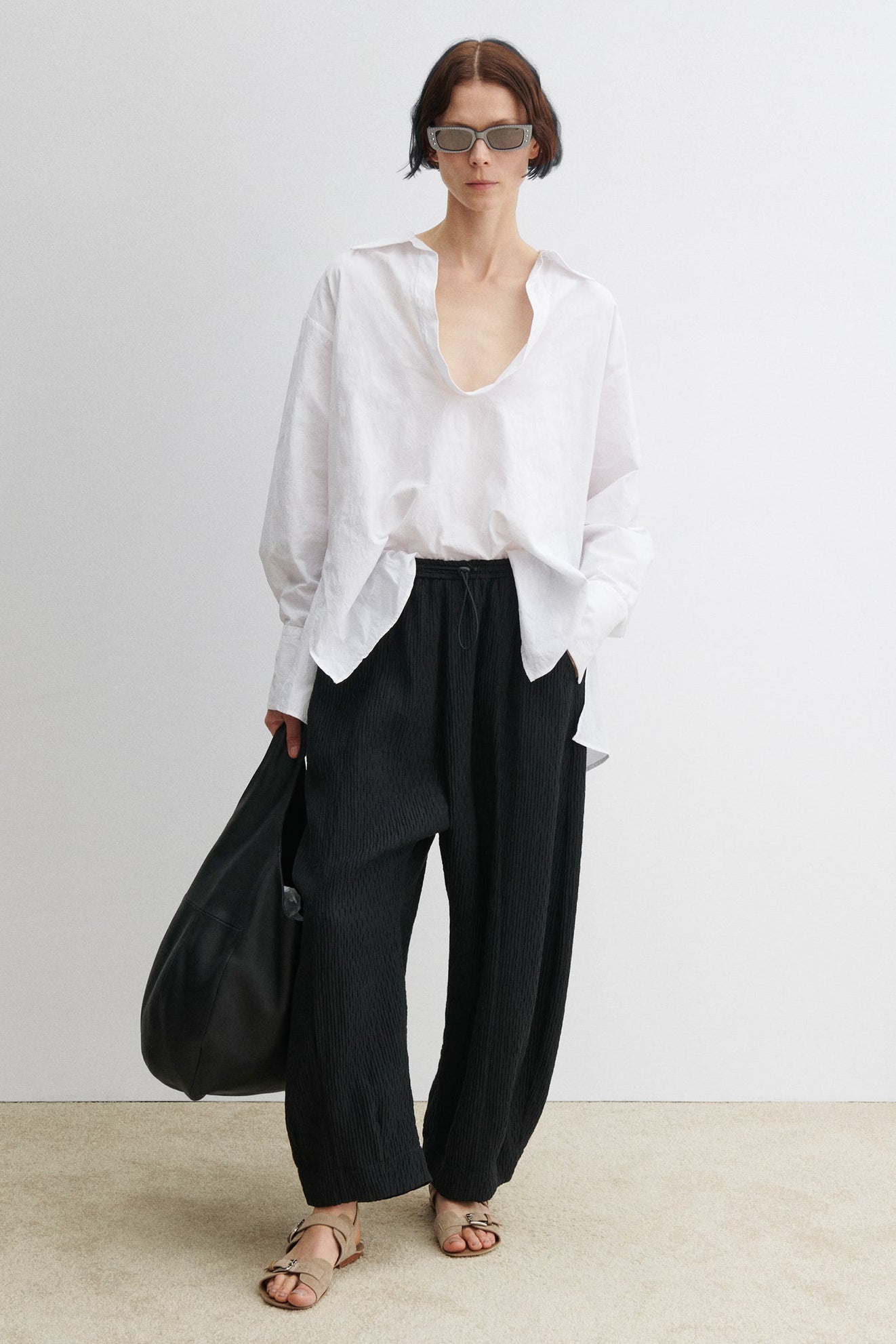 Full length front view of a woman wearing elevated casual and chic spring summer fashion in the Rachel Comey Black Ashbolt Pant featuring a relaxed wide-leg, elasticated drawstring waistband, two side seam pockets at an Alas Eius store. 