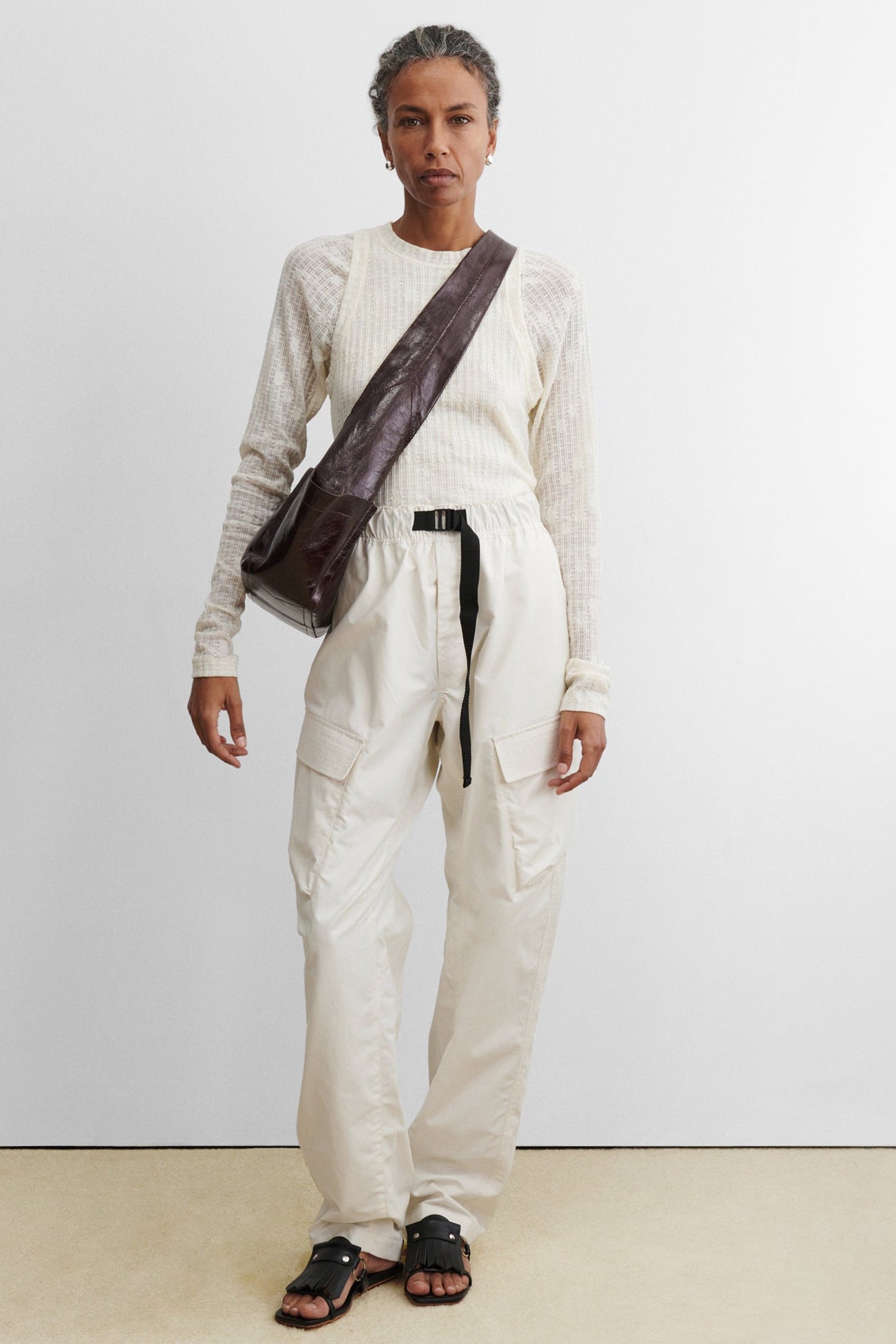 Woman wearing a modern and chic Rachel Comey Chestnut Leather Tool Bag featuring a fixed shoulder strap, extended exterior pockets, and magnetic closure. Can be worn over the shoulder or across the body at an Alas Eius store. Made in Italy. 