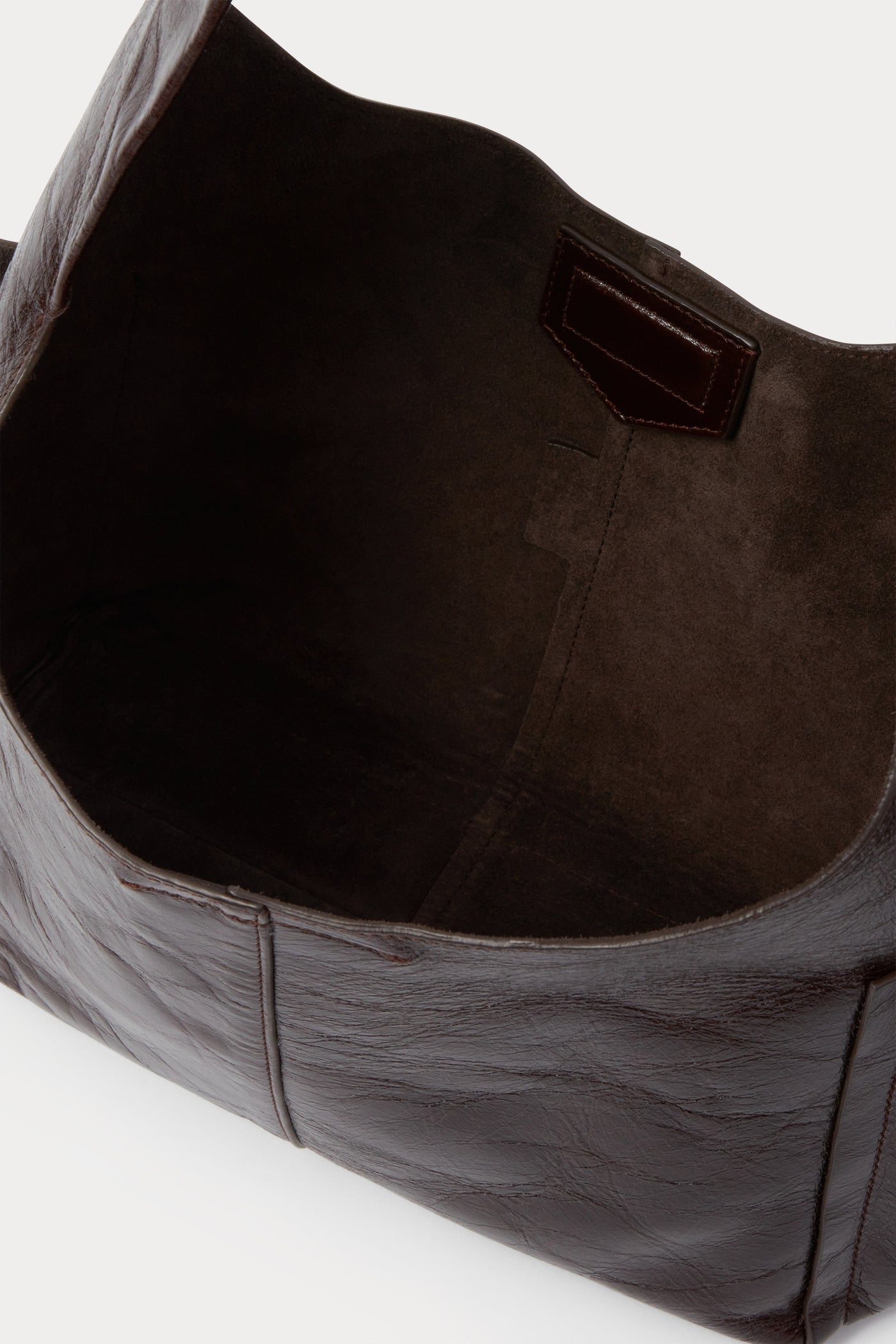 Close-up inside view of the sophisticated Rachel Comey Chestnut Leather Tool Bag featuring a fixed shoulder strap, extended exterior pockets, and magnetic closure. Can be worn over the shoulder or across the body at an Alas Eius store. Made in Italy. 
