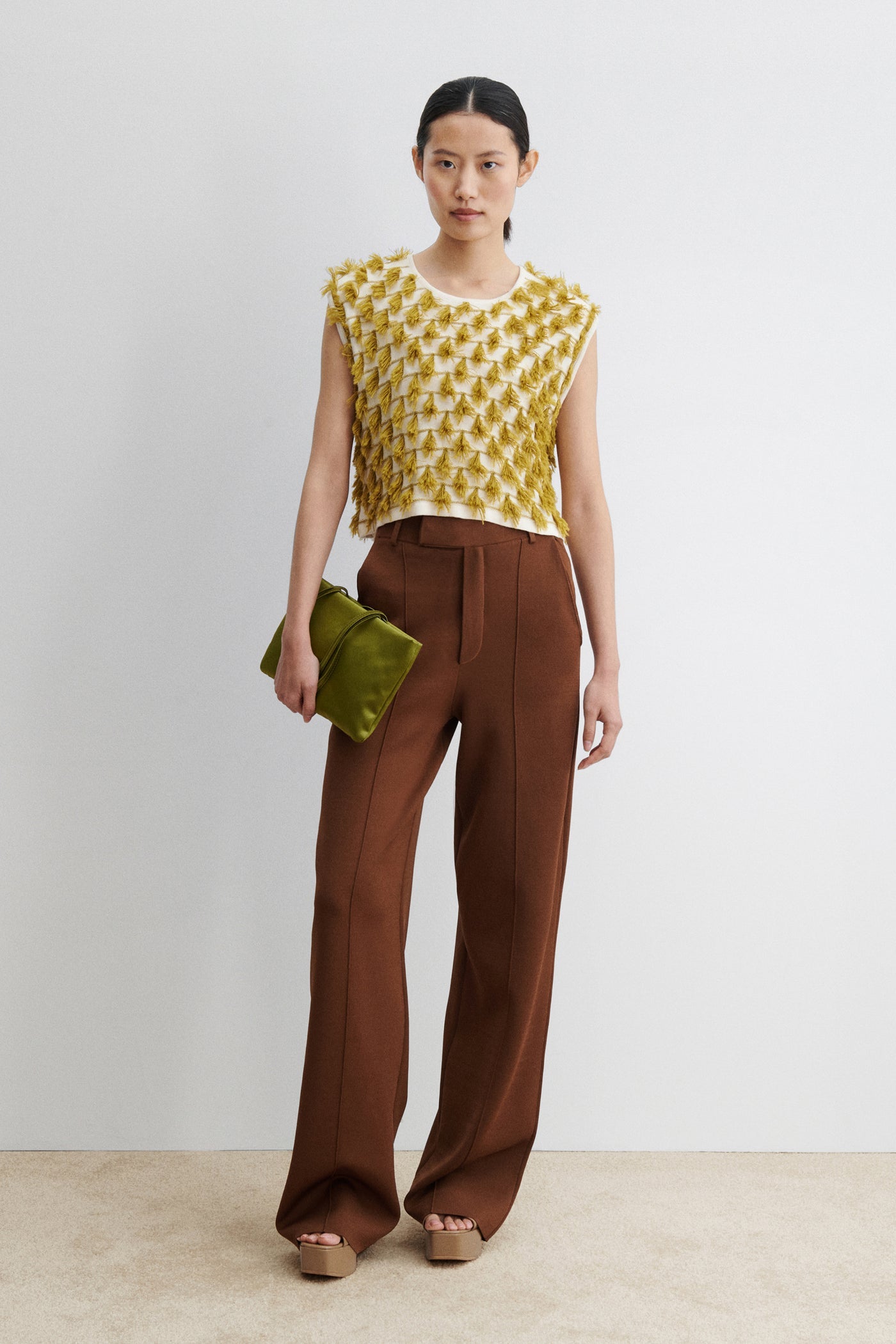 Woman posing wearing retro and vintage inspired fashion in a Rachel Comey Cotton and Baby Alpaca Cream Mustard Hazlitt sleeveless knit top detailed with rows of playful, three-dimensional fringes. Designed with a relaxed, boxy cut and finished with a soft crew neckline at Alas Eius. Made in Peru. 