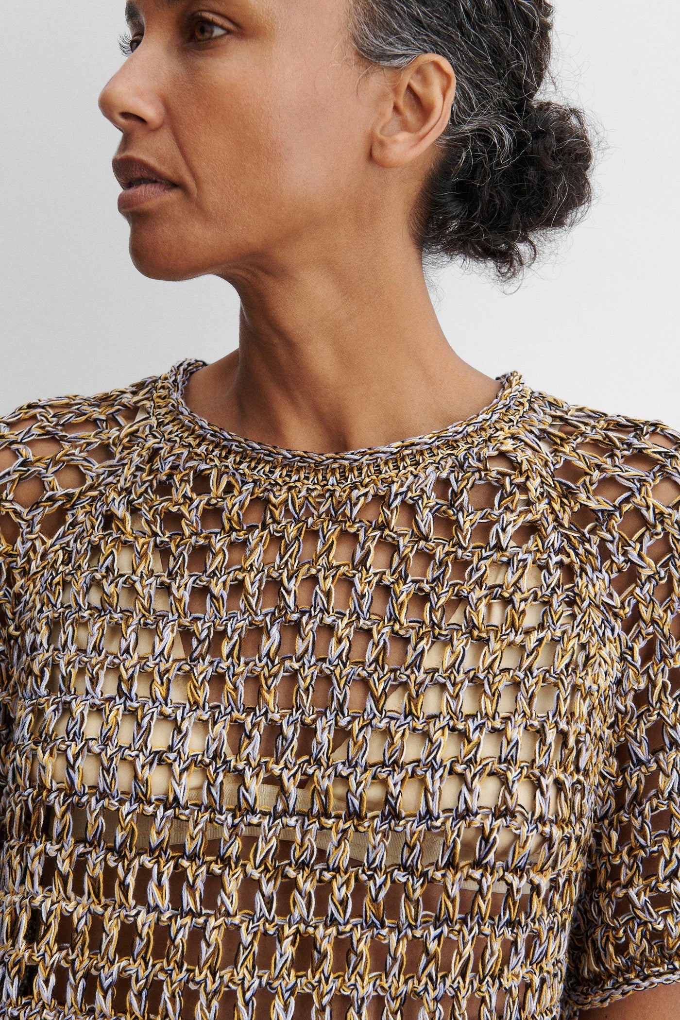 Close-up front view of a woman standing wearing spring fashion in the Rachel Comey Yellow Multi Drax Tee featuring an open-knit design, crafted from plies of colorful cotton, featuring a classic crew neckline and rolled edges. Designed with a relaxed fit for easy layering at an Alas Eius store. 