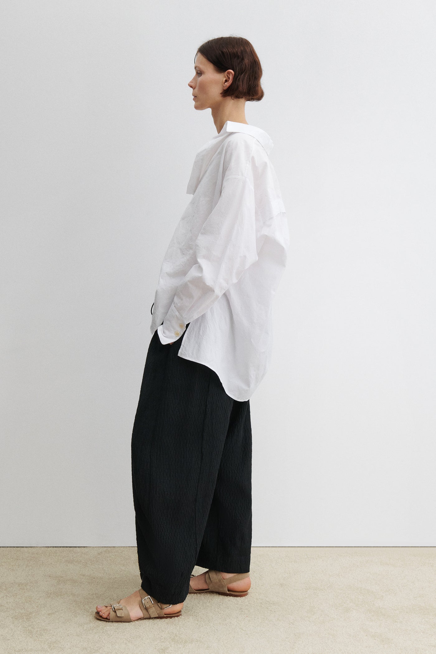 Full length side view of a woman wearing modern minimalist spring summer fashion in the Rachel Comey Black Ashbolt Pant featuring a relaxed wide-leg, elasticated drawstring waistband, two side seam pockets at an Alas Eius store. 