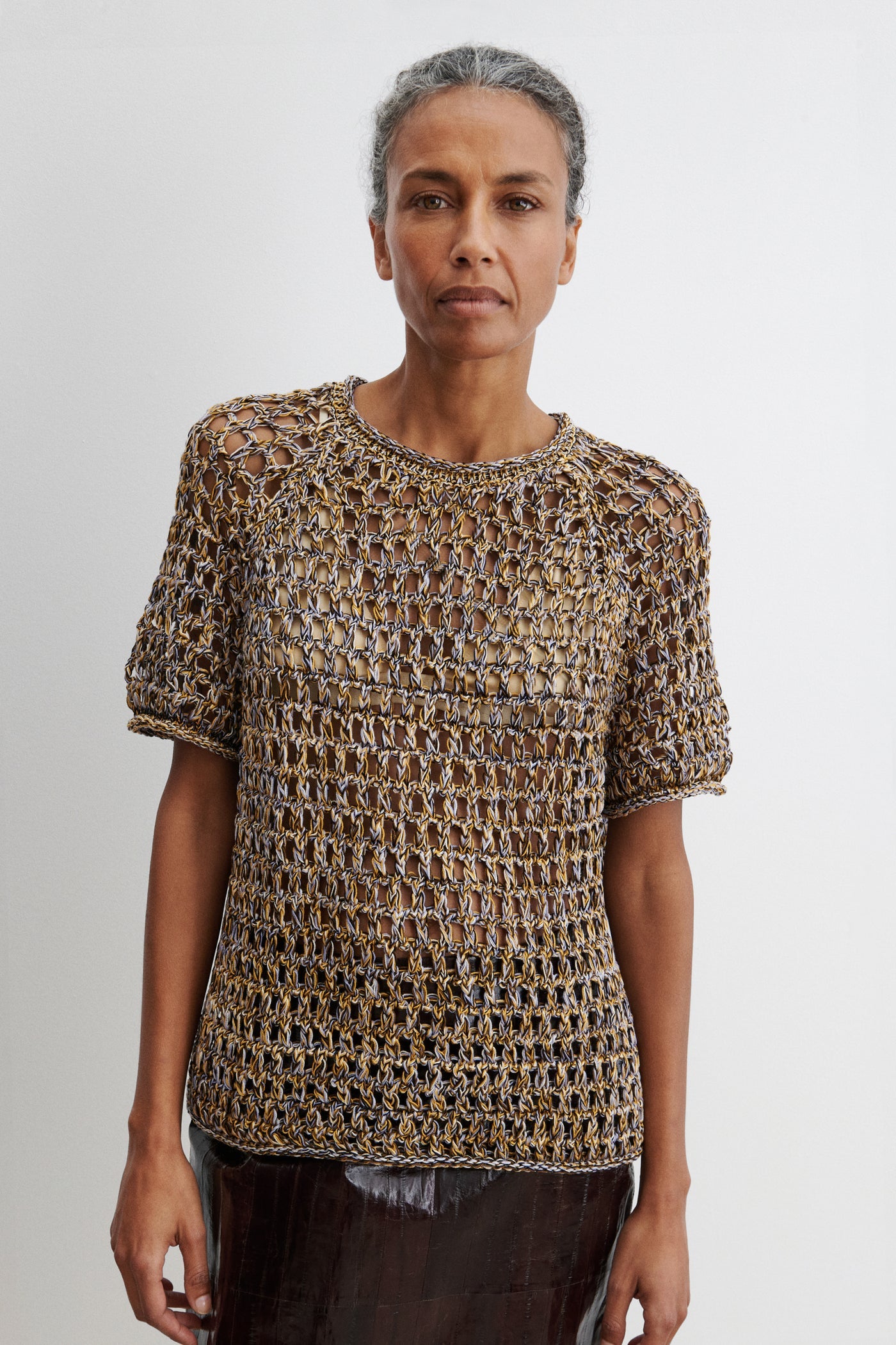 Close-up front view of a woman standing wearing spring fashion in the Rachel Comey Yellow Multi Drax Tee featuring an open-knit design, crafted from plies of colorful cotton, featuring a classic crew neckline and rolled edges. Designed with a relaxed fit for easy layering at an Alas Eius store. 