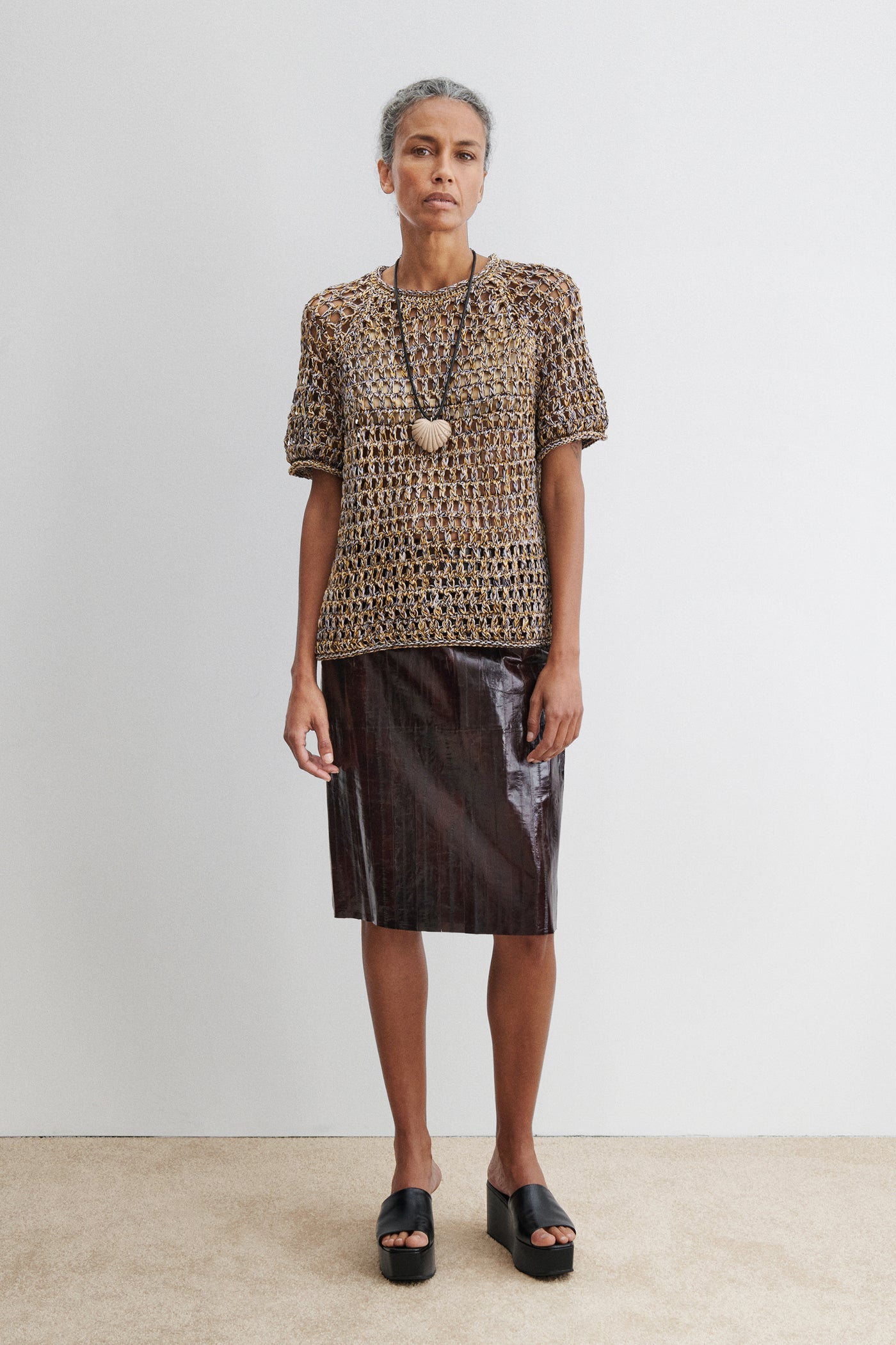 Woman standing wearing spring fashion in the Rachel Comey Yellow Multi Drax Tee featuring an open-knit design, crafted from plies of colorful cotton, featuring a classic crew neckline and rolled edges. Designed with a relaxed fit for easy layering at an Alas Eius store. 