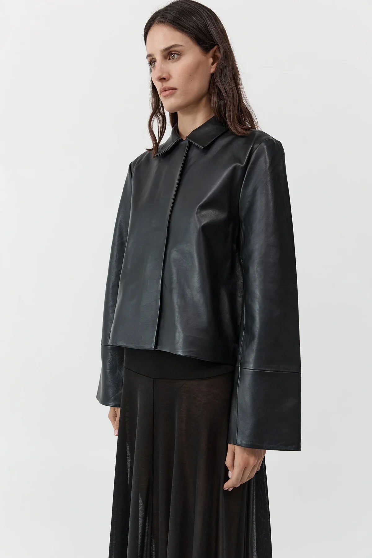 3/4 view of a woman wearing St. Agni Black Leather Minimal Jacket with concealed magnetic buttons for a seamless closure and wide cuff sleeves at Alas Eius. 