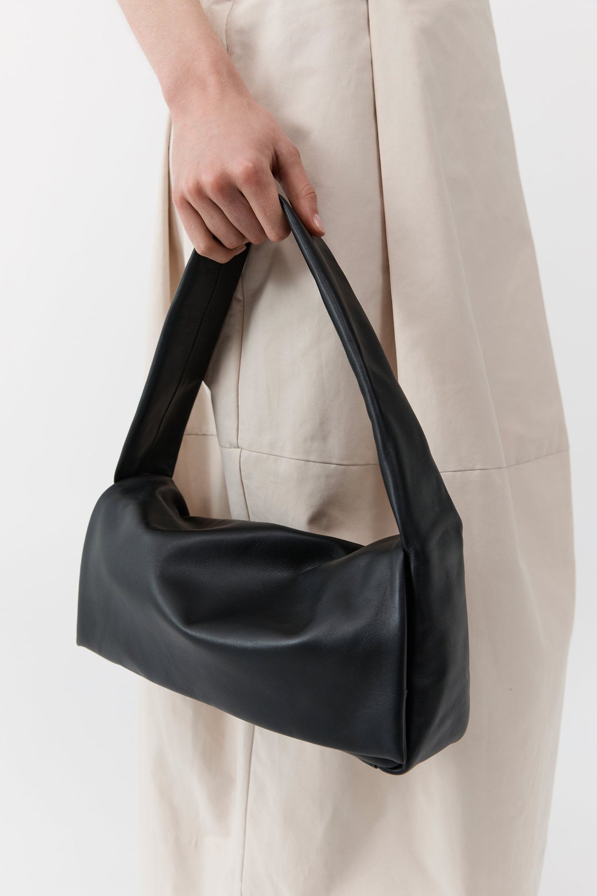 Close-up detail view of a woman holding a St. Agni black leather soft slim satchel bag which is lined with cotton canvas and features a magnetic closure at Alas Eius.