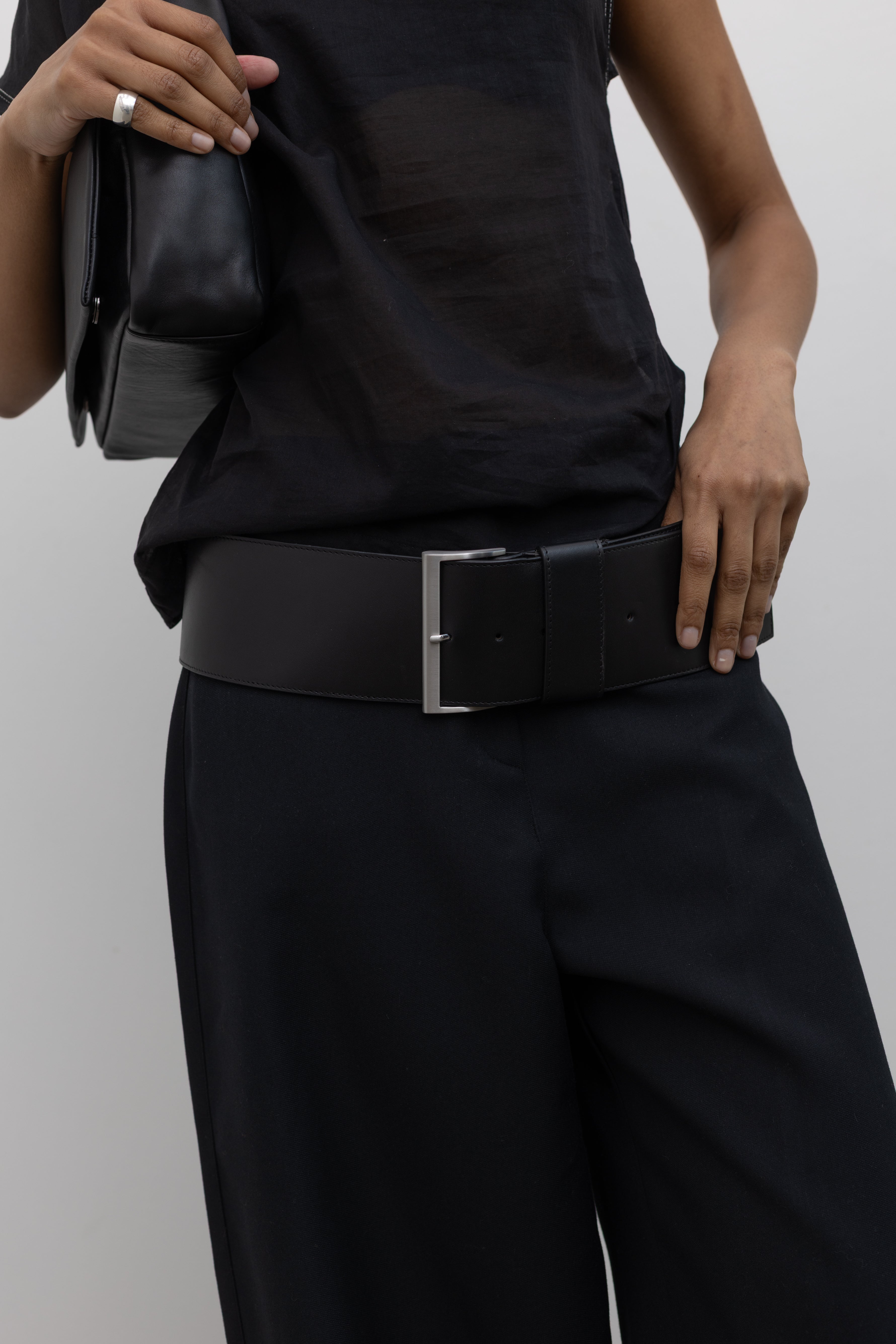 Close-up view of a Woman wearing a sleek and sophisticated St. Agni Black Leather Wide Classic Belt with a brushed silver rectangular buckle paired with a black outfit at Alas Eius.