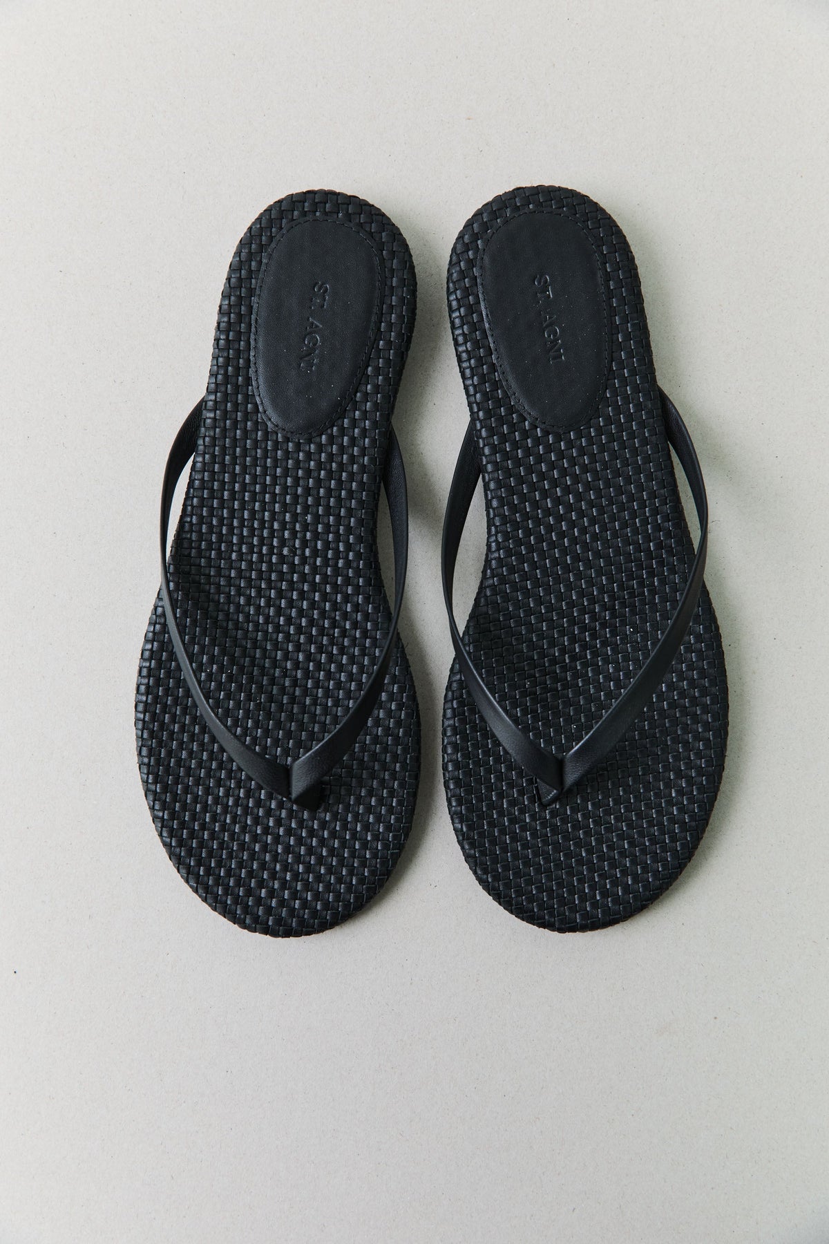Close-up product view of a pair of St. Agni Black Leather Woven Thong Flip Flops at Alas Eius