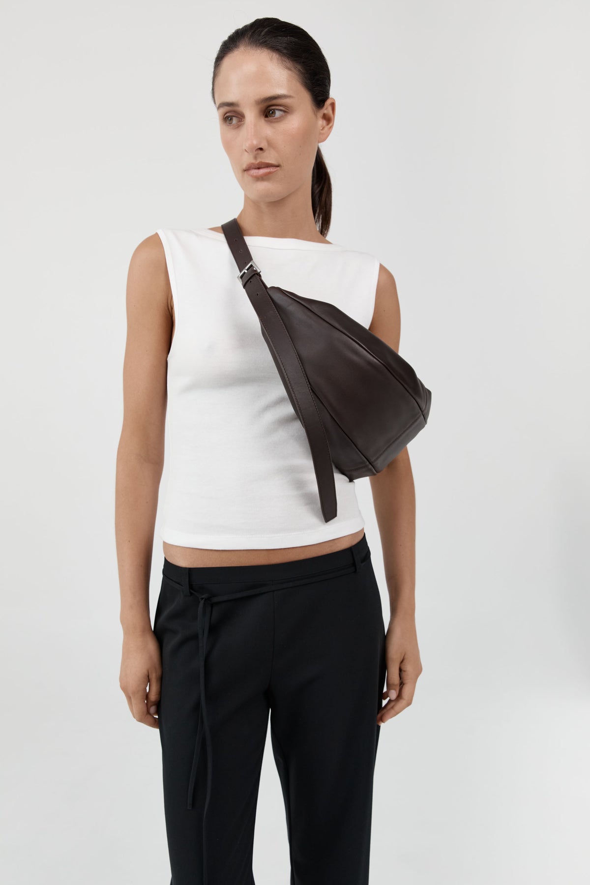 Woman wearing elevated essential in a minimalist St.Agni Coffee brown leather Adjustable strap Slim Crescent shaped Bag at Alas Eius