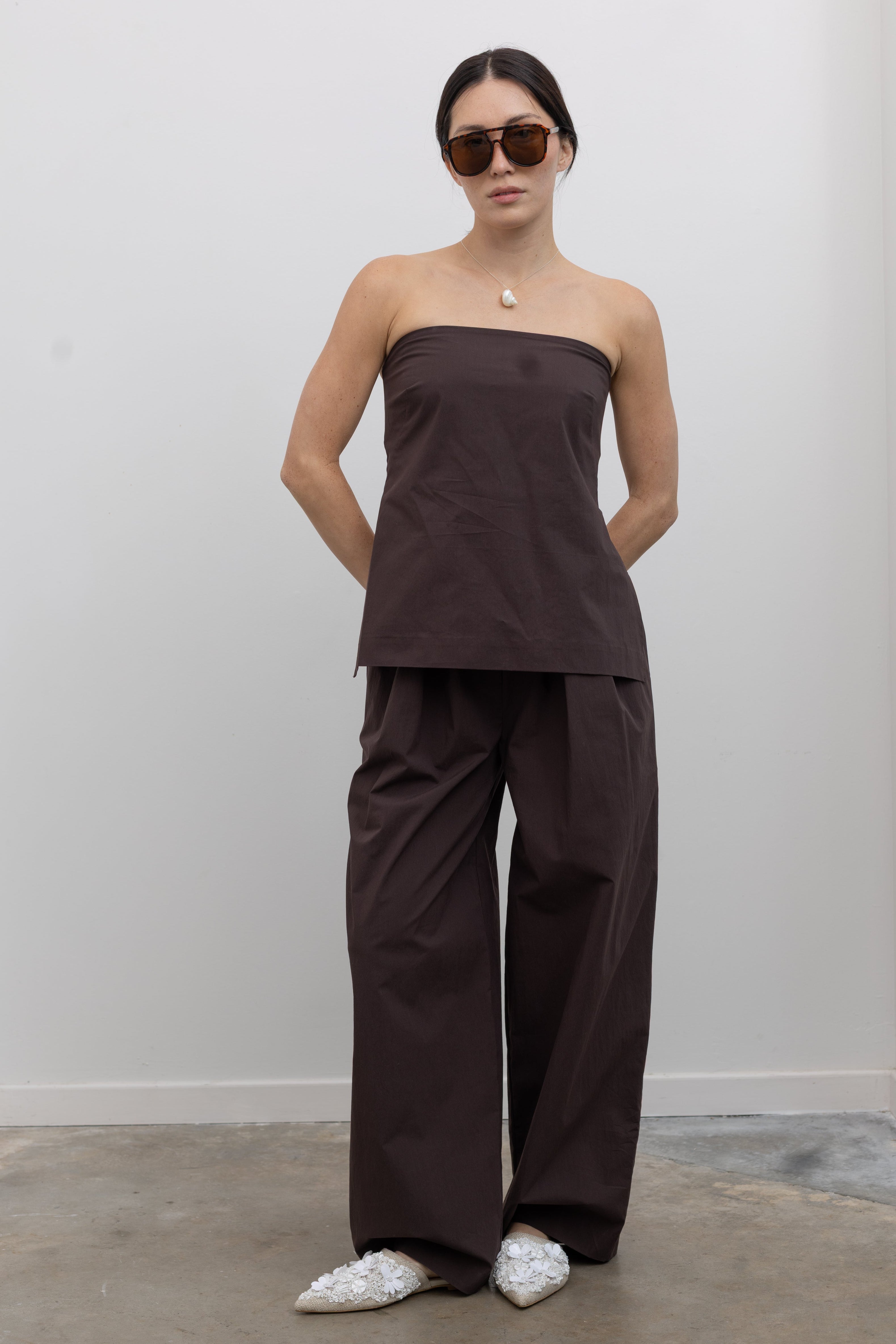 Full front view of a woman standing wearing Spring and Summer fashion in the St. Agni Bark Relaxed Pleat Pants featuring a mid-rise waist and a gently tapered leg at Alas Eius.