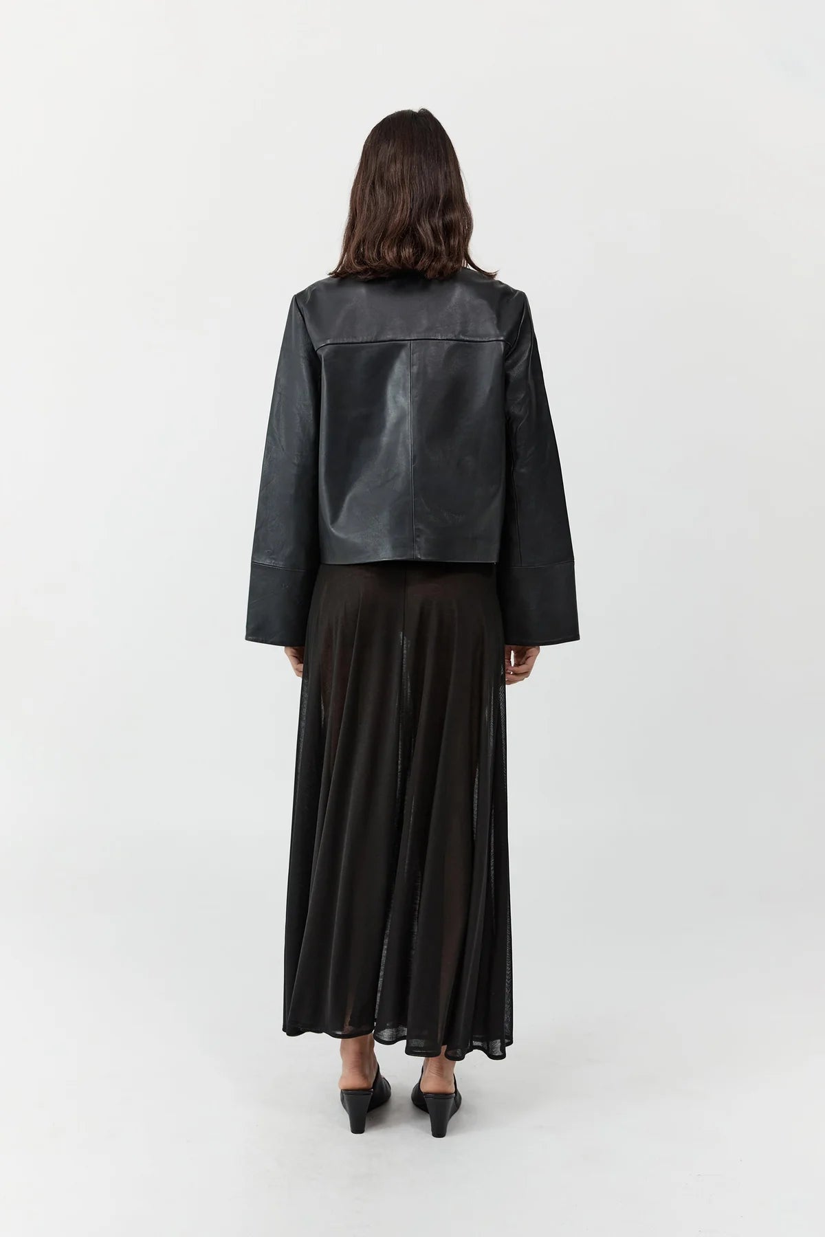 Back view of a woman wearing St. Agni Black Leather Minimal Jacket with concealed magnetic buttons for a seamless closure and wide cuff sleeves at Alas Eius. 