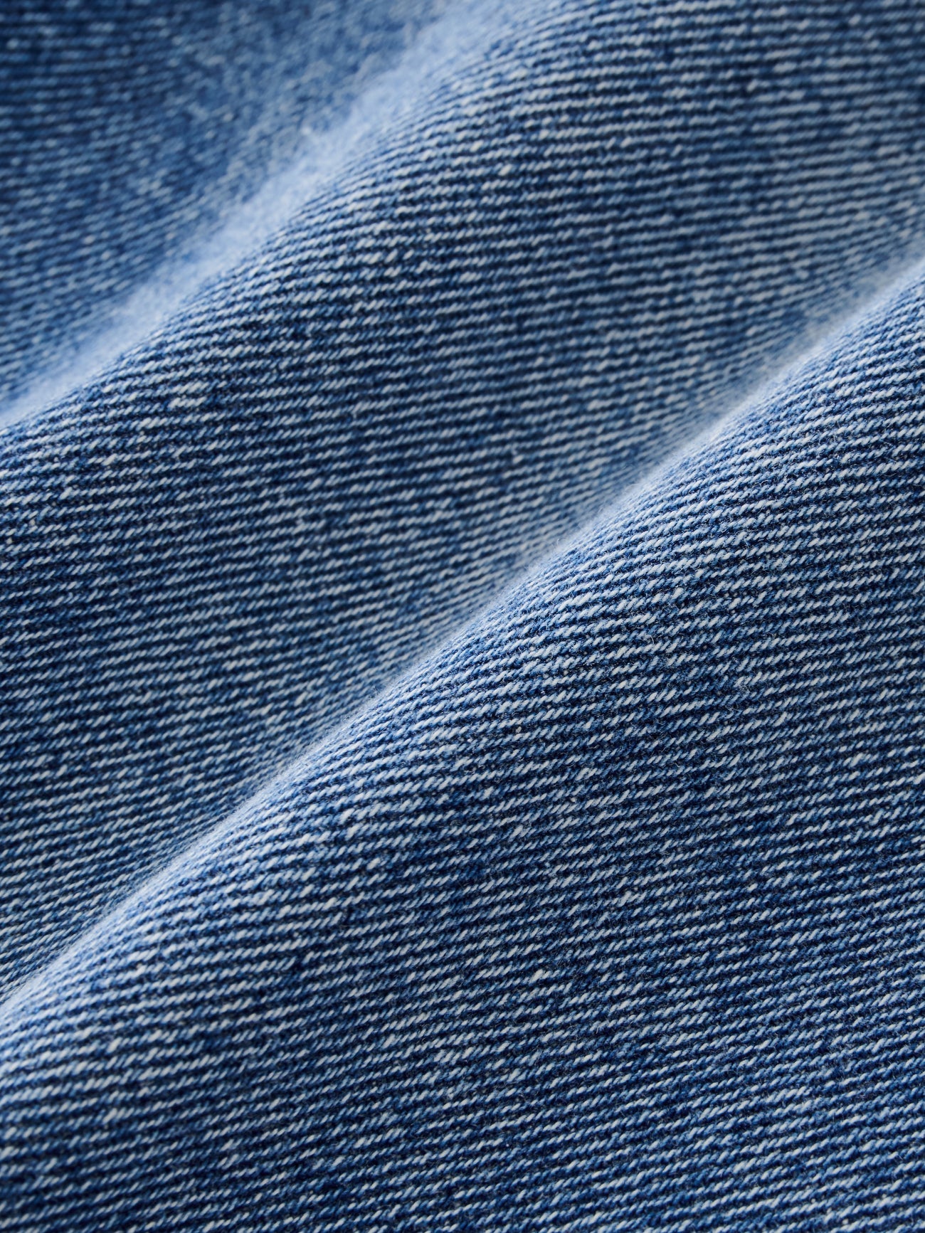 Close-up view of regenerative cotton denim used to make the Studio Nicholson Worn Wash Indigo Chalco Wide Crop Denim Jeans at Alas Eius. 
