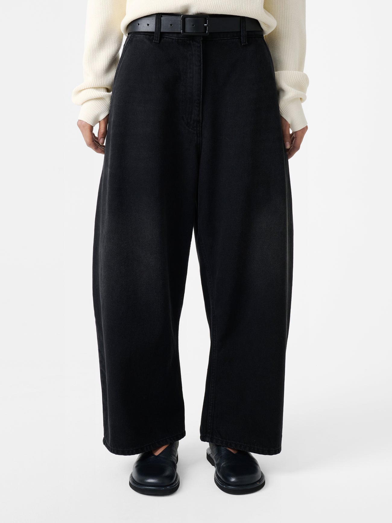 Close-up front view of a woman wearing elevated casual weekend essential style in the Studio Nicholson Washed Black Chalco Wide Crop Denim Pant that are cut wide and cropped, with a curved leg and dropped crotch at Alas Eius. They are constructed from a denim that’s been woven from regenerative cotton and made in the UK. 