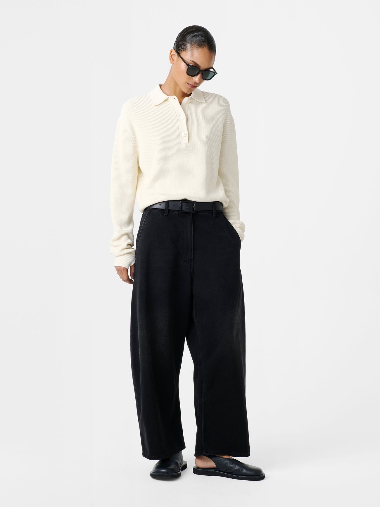 Woman standing wearing an elevated classic and wardrobe staple in the Studio Nicholson Washed Black Chalco Wide Crop Denim Pant that are cut wide and cropped, with a curved leg and dropped crotch. They are constructed from a denim that’s been woven from regenerative cotton and made in the UK. 