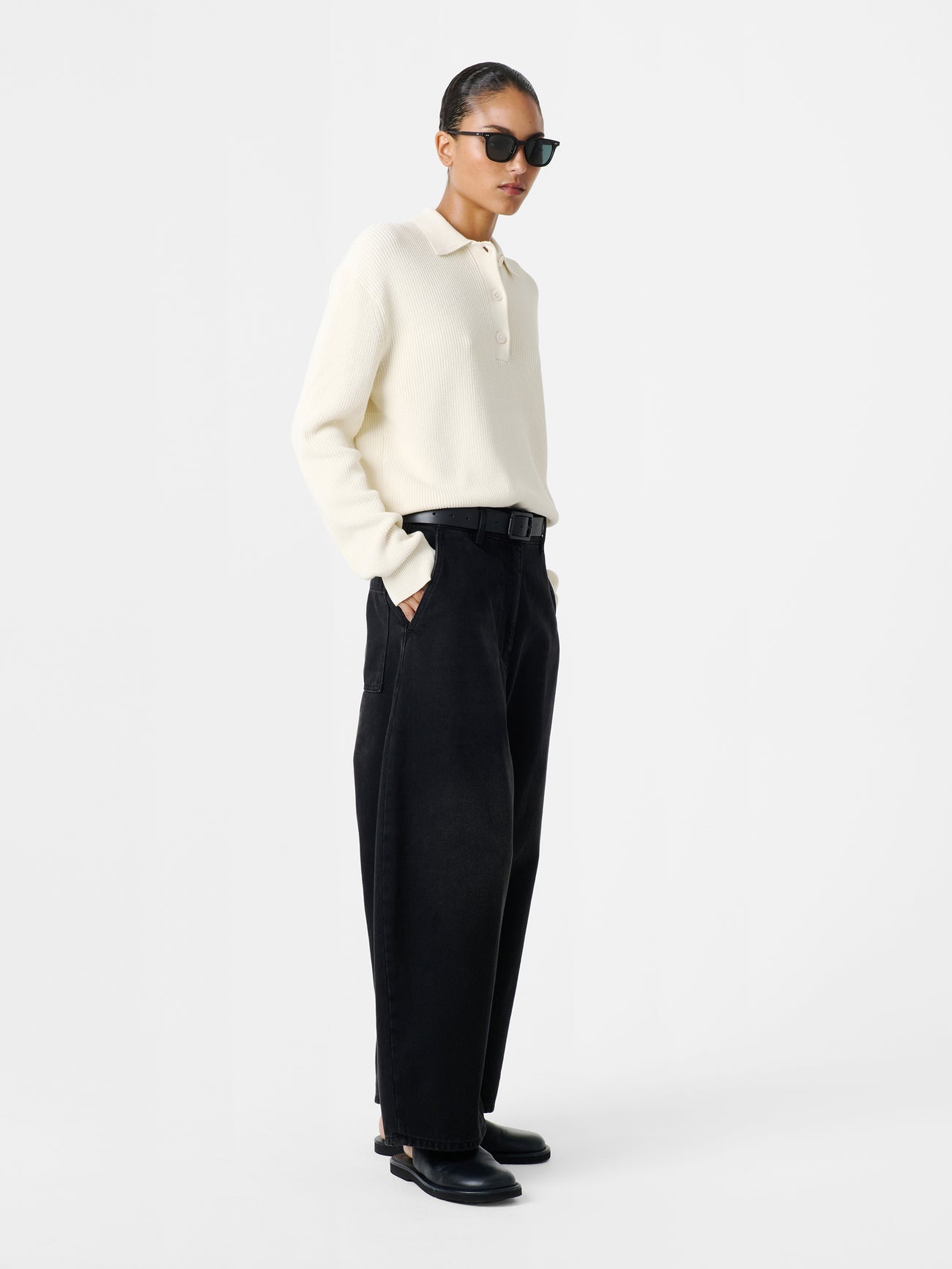 Woman standing wearing an elevated classic and wardrobe staple in the Studio Nicholson Washed Black Chalco Wide Crop Denim Pant that are cut wide and cropped, with a curved leg and dropped crotch. They are constructed from a denim that’s been woven from regenerative cotton and made in the UK. 