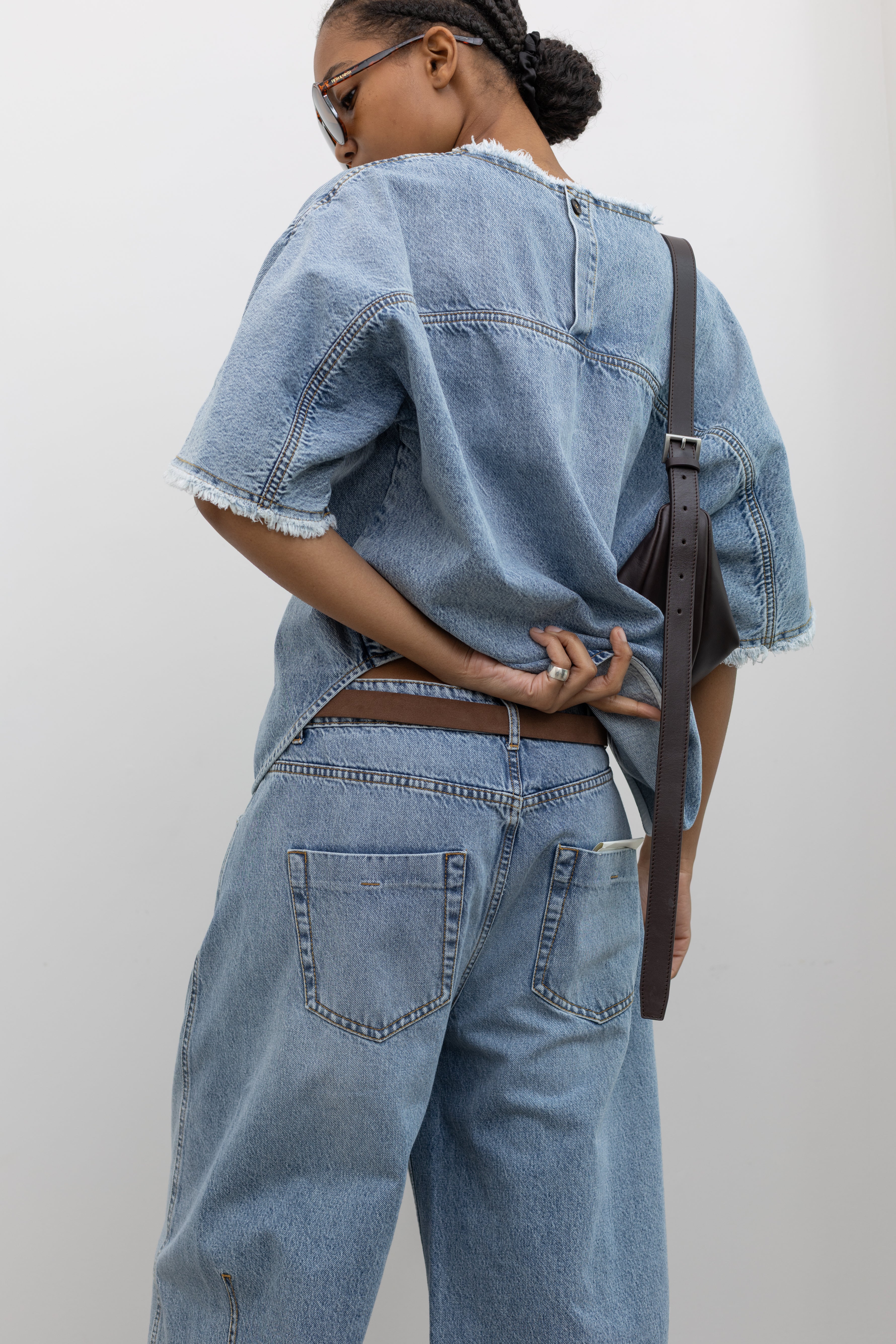 Close-up back view of a woman wearing cool relaxed fit Tela brand light-blue wash baggy wide leg denim jeans with classic patch pockets and strappy sandals at an Alas Eius store. 