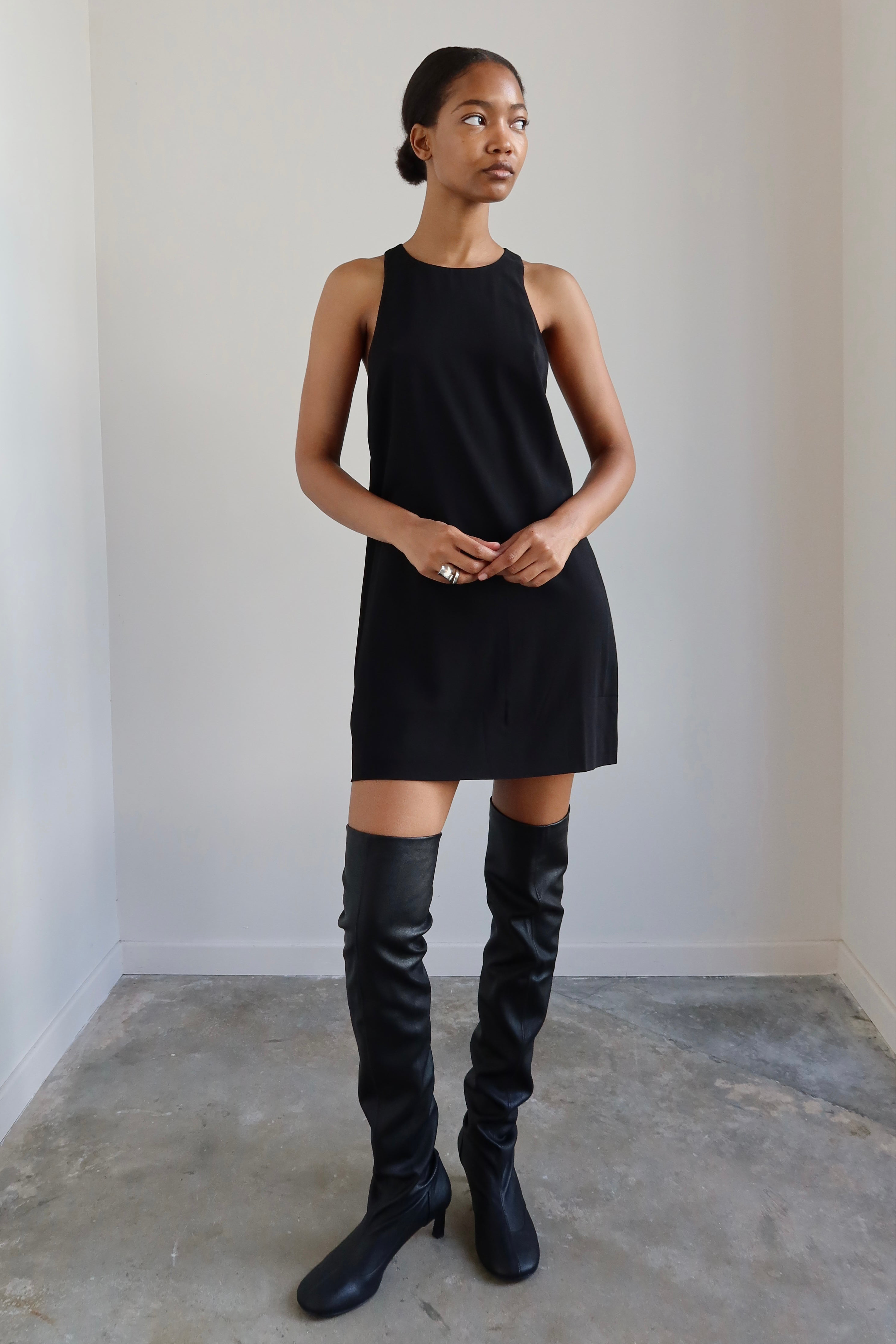 Woman wearing Tela Macob Black Leather over-the-knee Heeled slouchy Boots paired with a little black racerback dress at Alas Eius