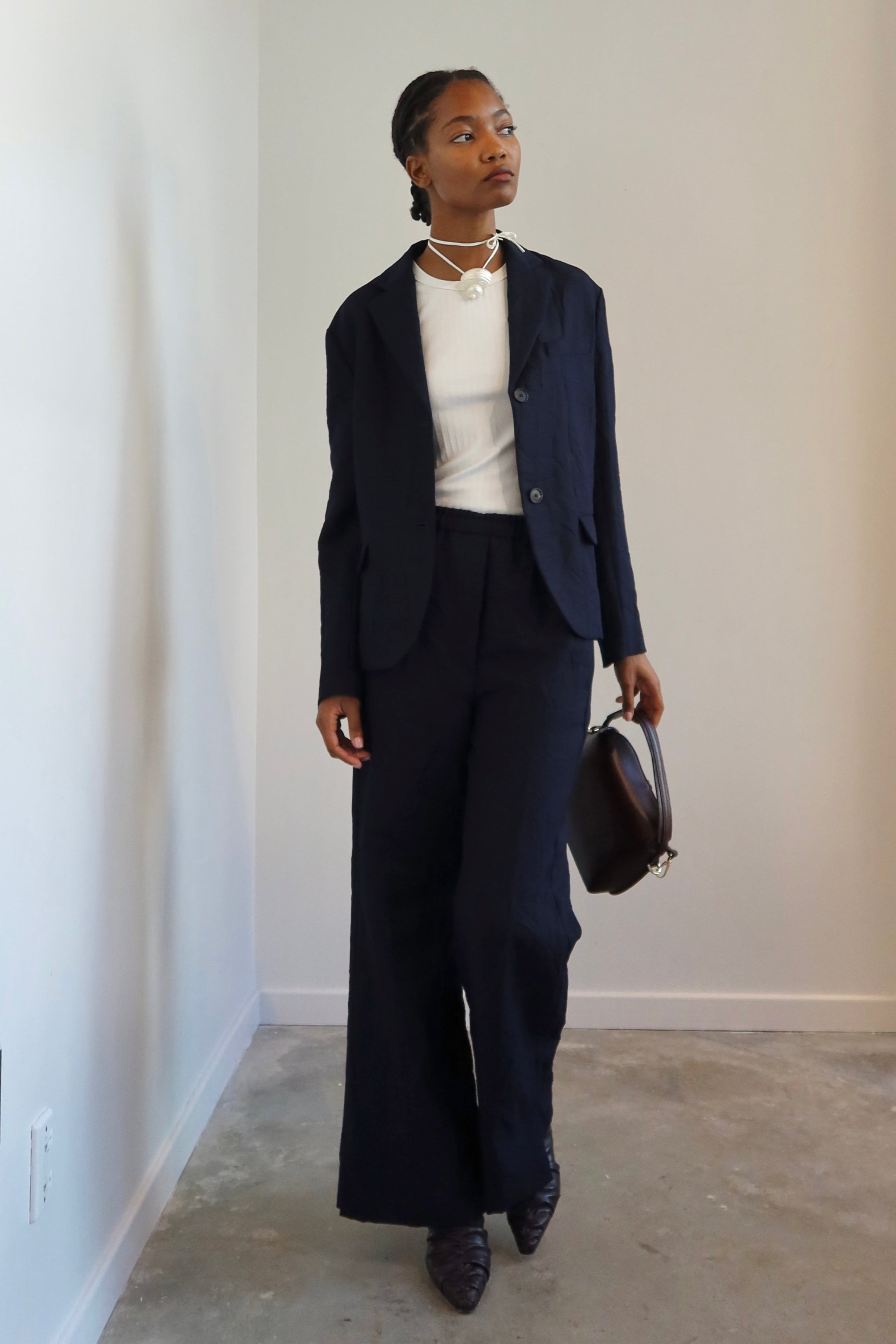 Woman standing wearing Tela Radio Midnight Tailored Trousers featuring  an intentionally crinkled texture, elastic waistband, hidden drawstring, Mid-rise waist, and a slim fitting leg at Alas Eius.