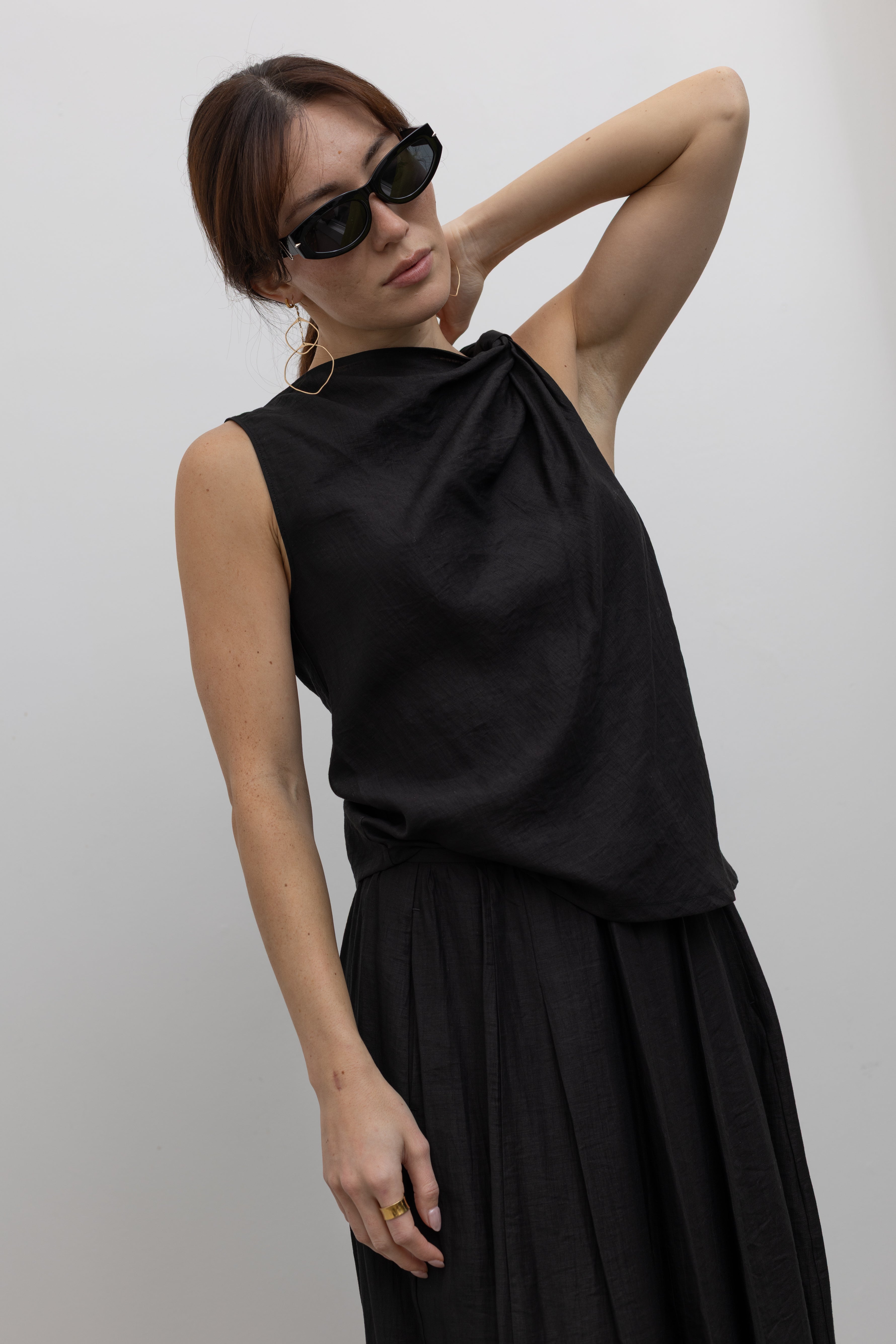 Front view of a woman posing wearing Spring fashion in an elegant and flattering Tela Cody black linen knotted shoulder sleeveless top at Alas Eius. 