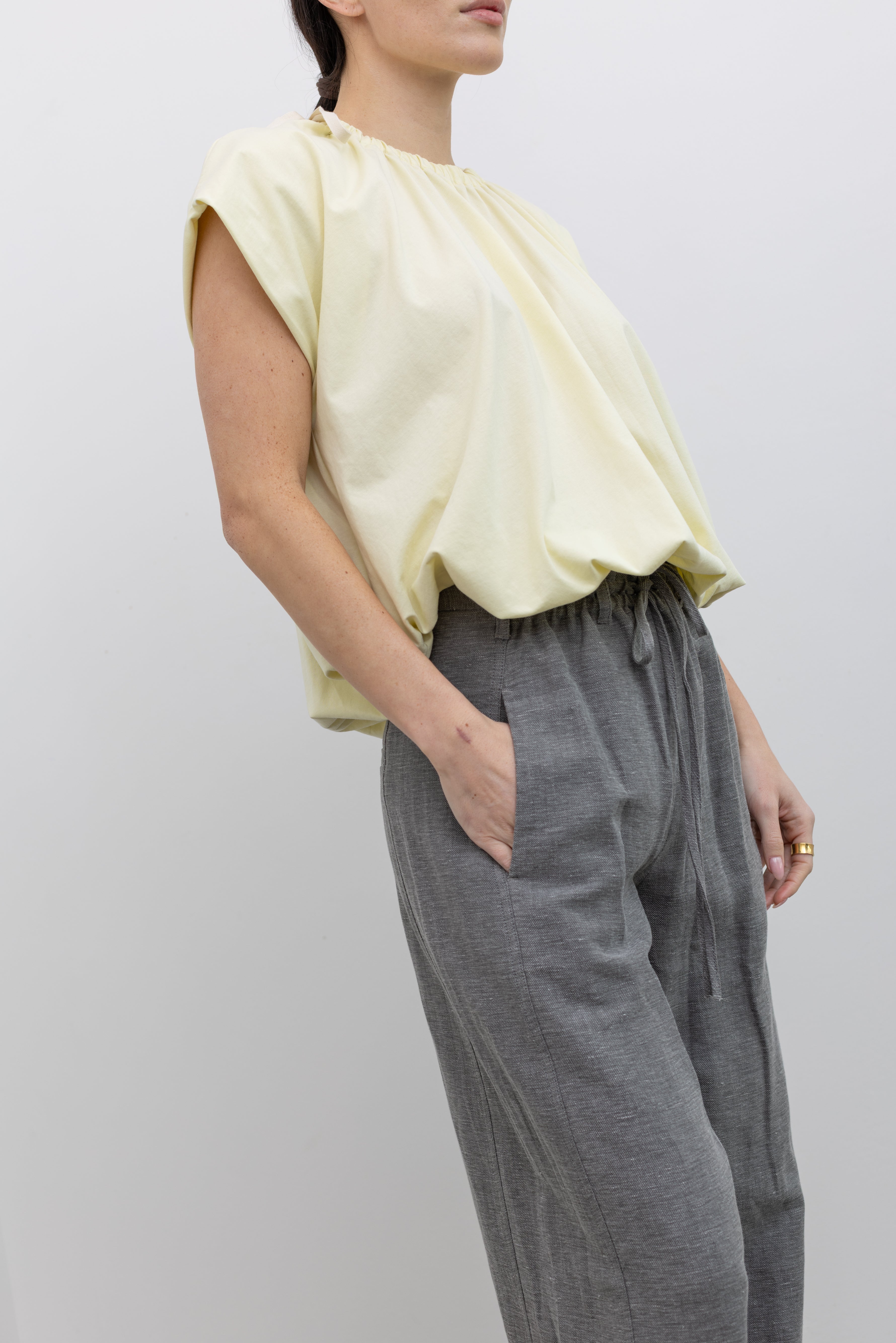 3/4 view of a woman wearing modest spring fashion in a Tela Light Yellow Gathered Neck Bubble Hem Top and Tela Lucio light gray drawstring pants featuring a wide leg and side seam pockets at an Alas Eius store. 