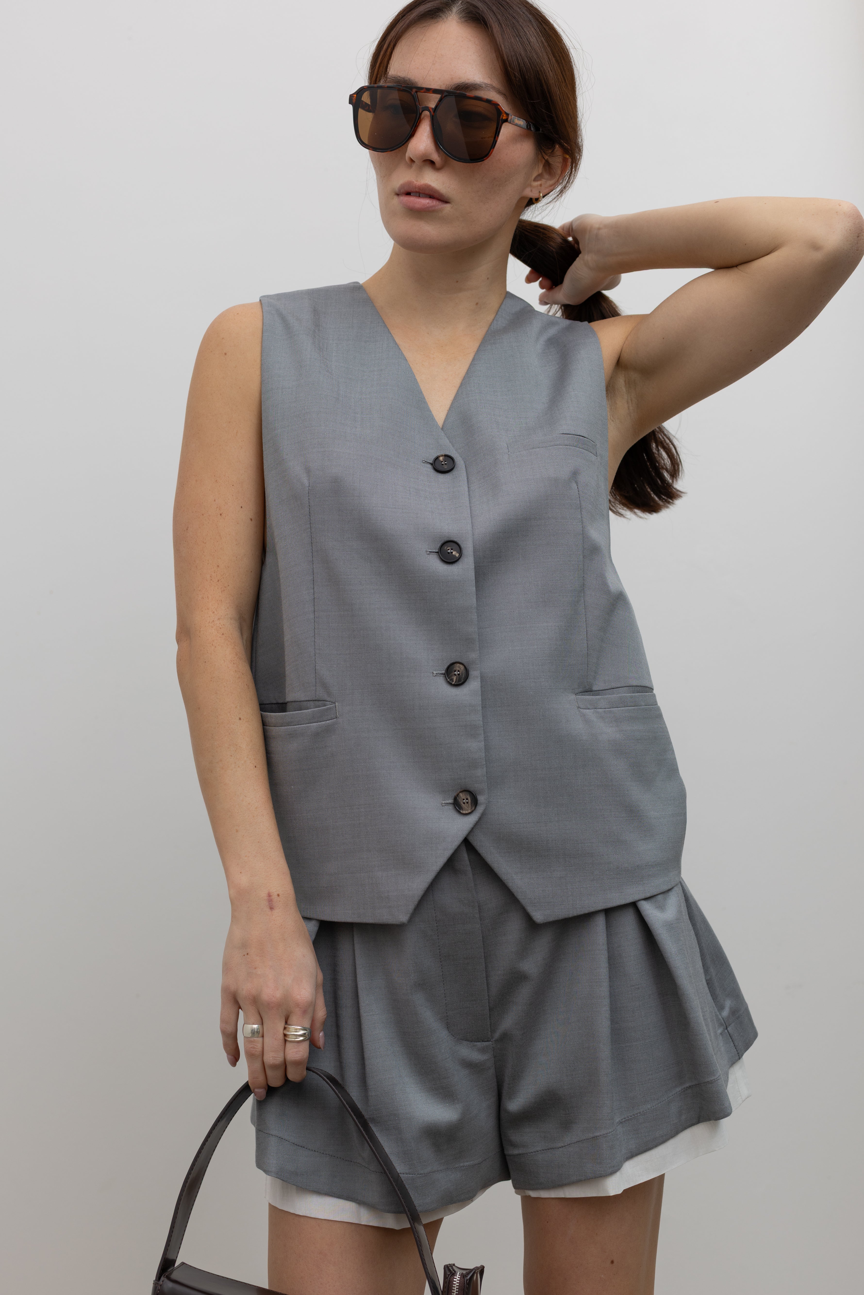 Woman posing wearing Spring fashion in a sophisticated and refined Tela Gabriel Grey Cool Wool Button Down Vest paired with Tela grey wool layered wool shorts at Alas Eius.