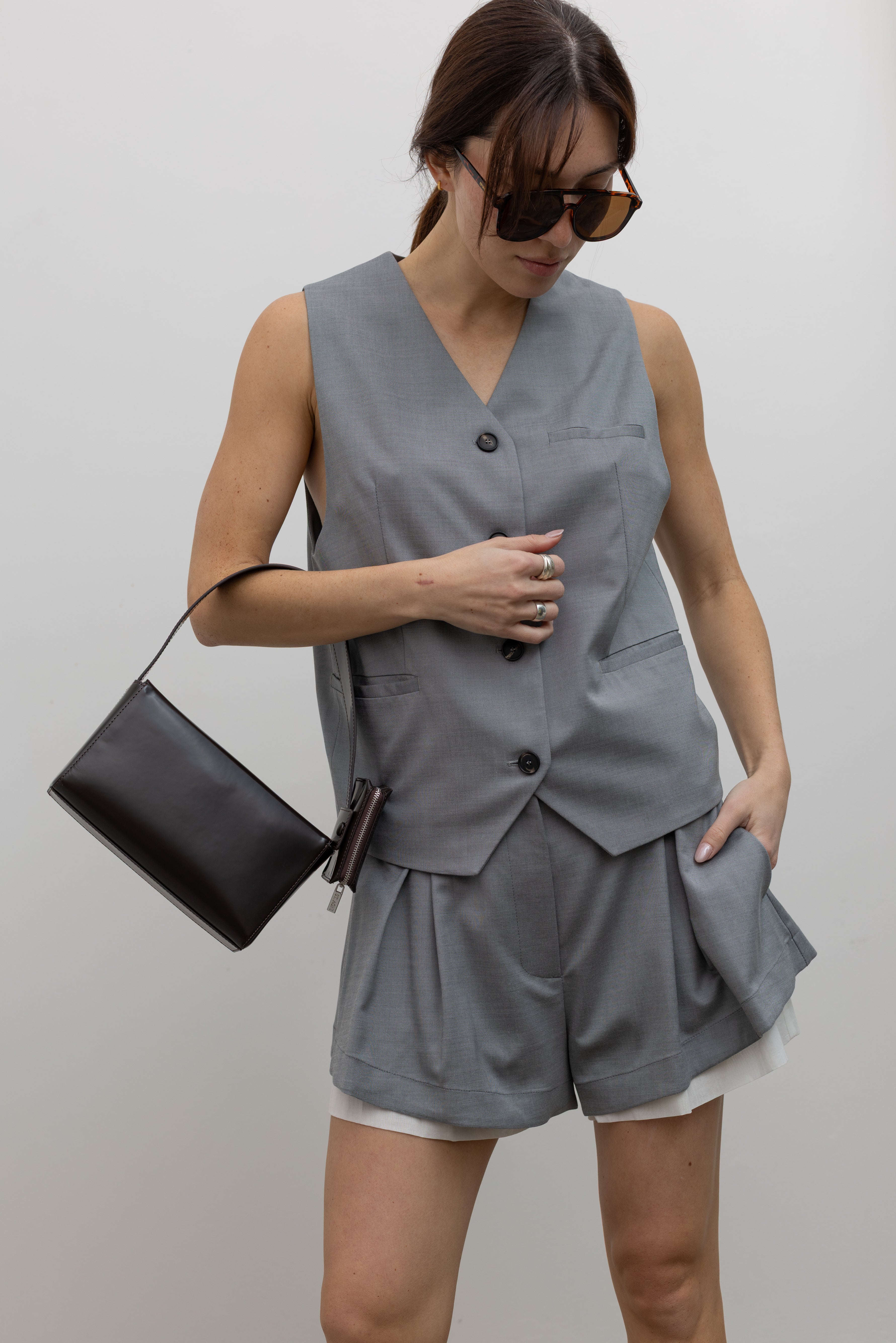 Woman at Alas Eius wearing Spring fashion in a Tela Gabriel Cool Wool Grey Vest paired with  Tela grey cool wool shorts that feature soft front pleating, a subtle white underlayer that peeks out at the hem, side pockets, a back patch pocket, and belt loops.