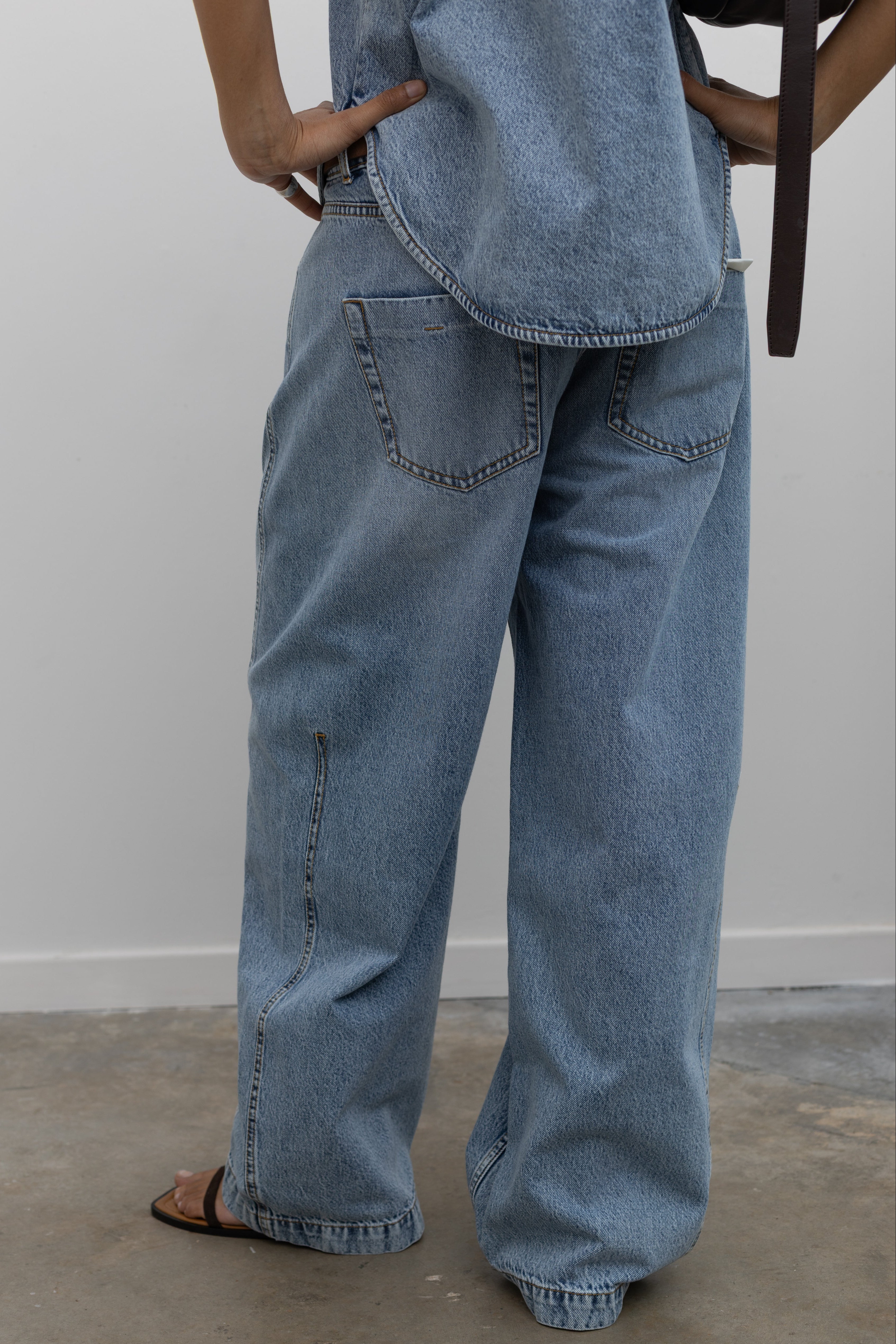 Close-up back view of a woman wearing cool relaxed fit Tela brand light-blue wash baggy denim jeans and strappy sandals at an Alas Eius store. 