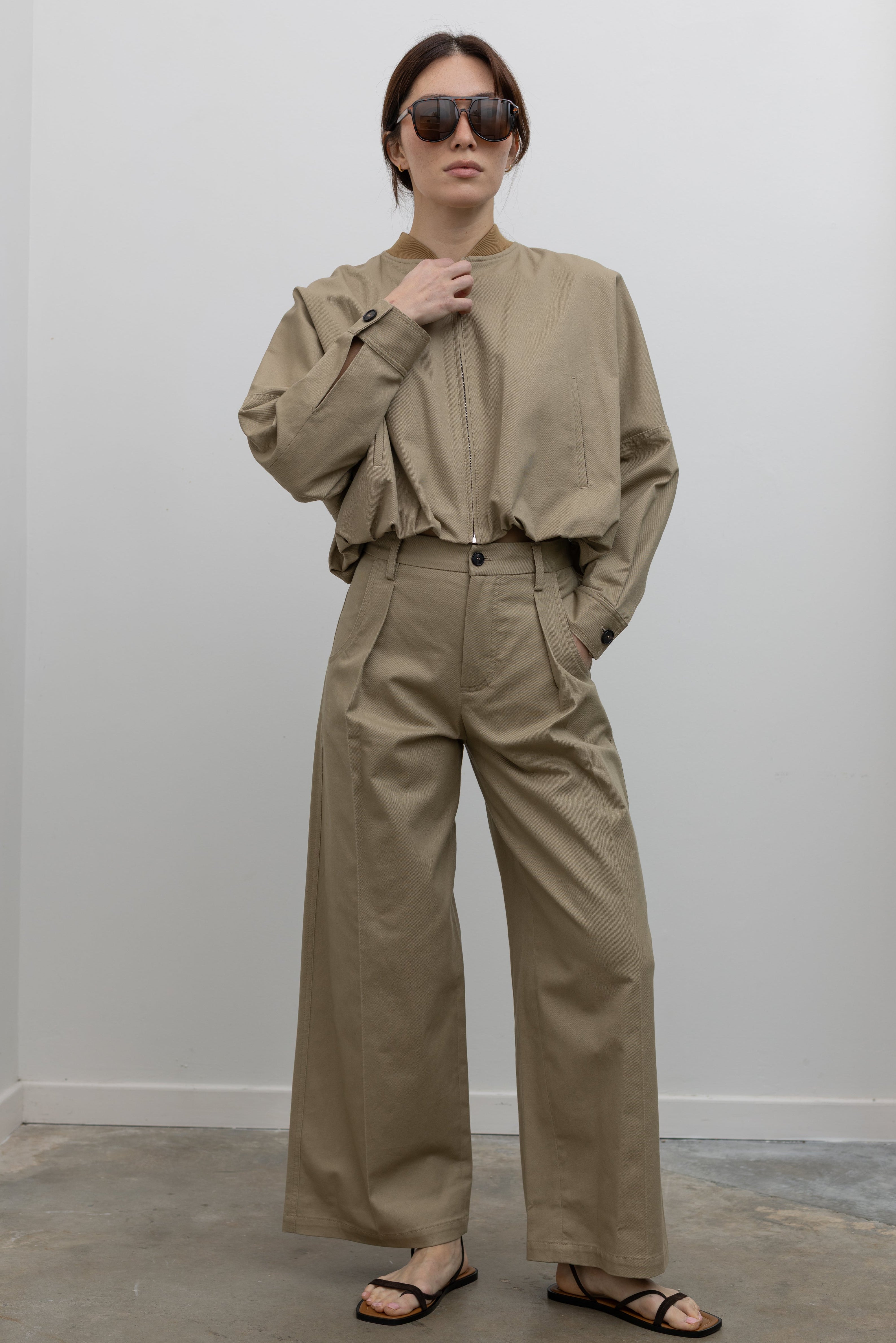 Woman standing wearing Spring fashion in a pair of Tela Rubicon Sand Cotton Gabardine Trousers and cropped jacket with sunglasses and sandals at Alas Eius