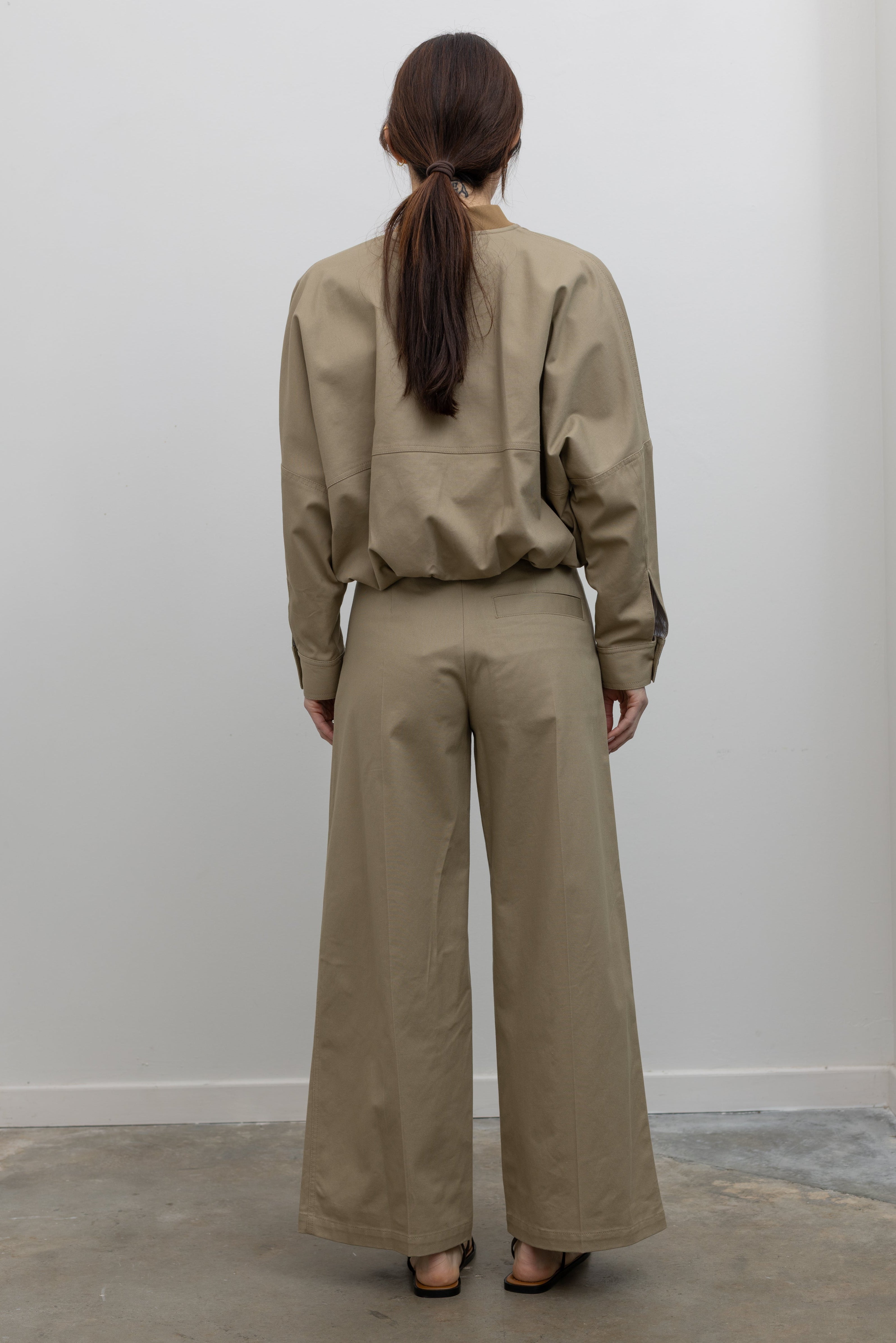 Back view of Woman standing wearing Spring fashion in a pair of Tela Rubicon Sand Cotton Gabardine Trousers and cropped jacket with sunglasses and sandals at Alas Eius