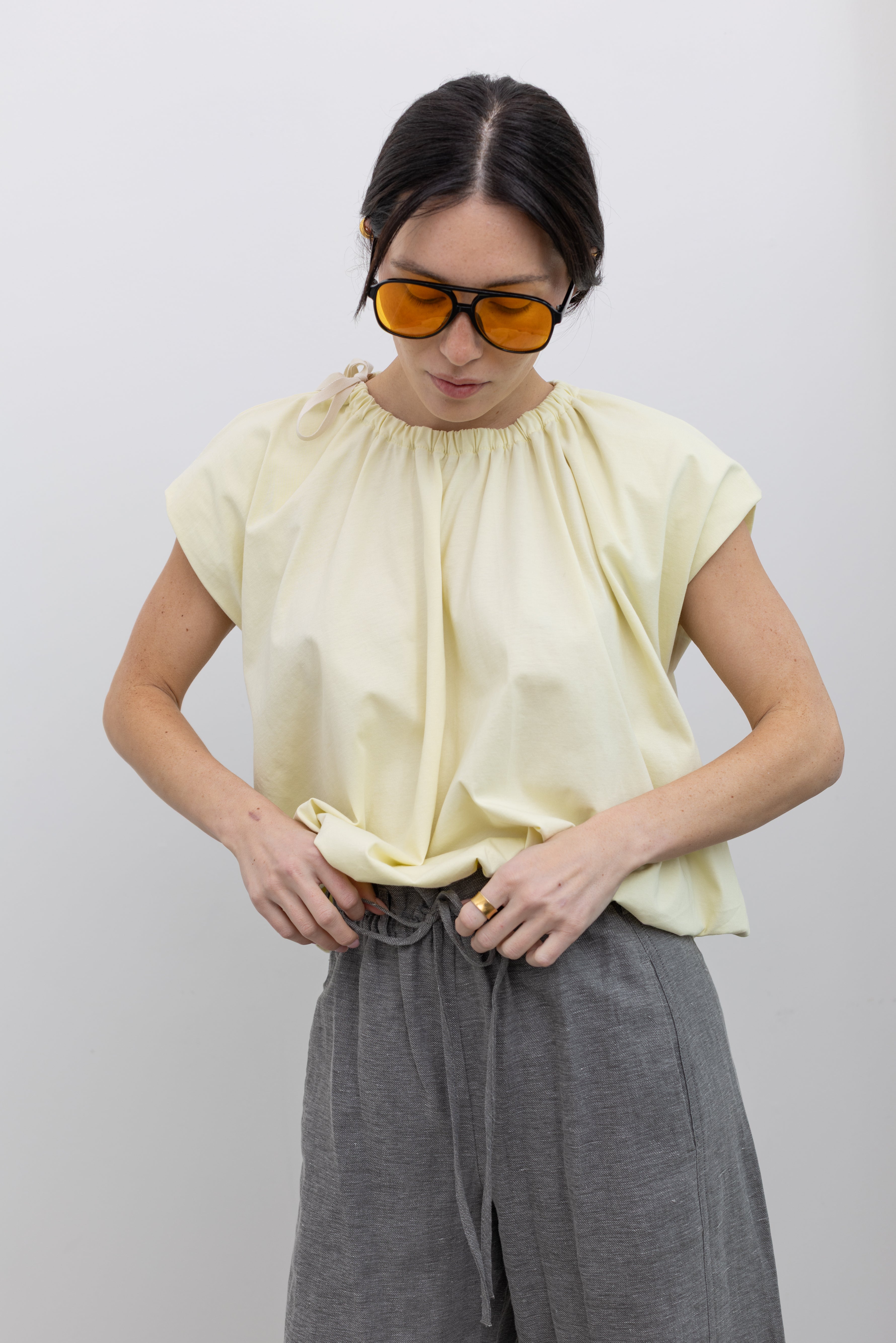 Close-up view of a woman wearing modest and chic spring fashion in a Tela pastel yellow gathered neck bubble hem short sleeve top at Alas Eius.
