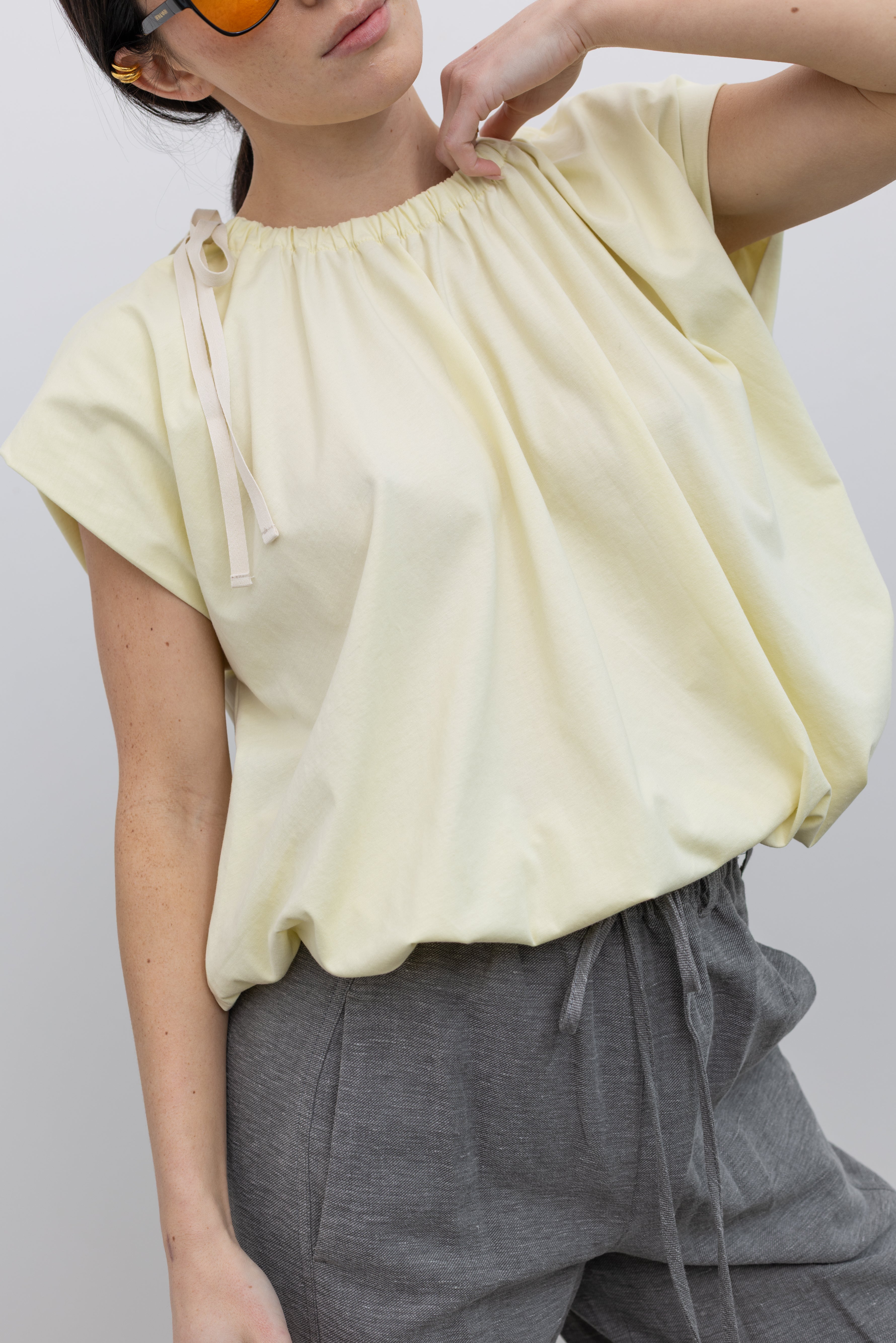 Close-up view of a woman wearing spring fashion in a Tela pastel yellow gathered neck bubble hem short sleeve top at Alas Eius.