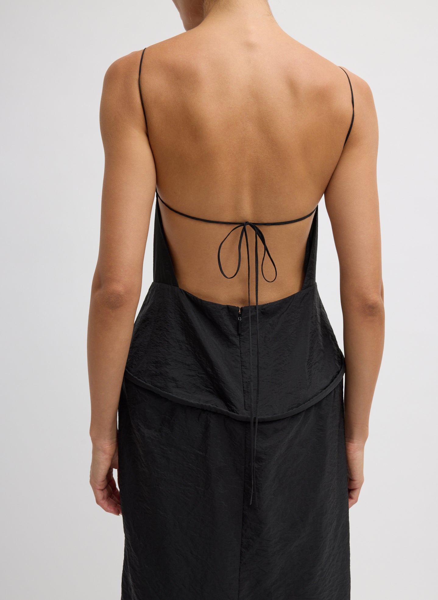 Detailed back view of a woman wearing Spring fashion in a black strappy chassis hoop open back dress by Tibi at Alas Eius 