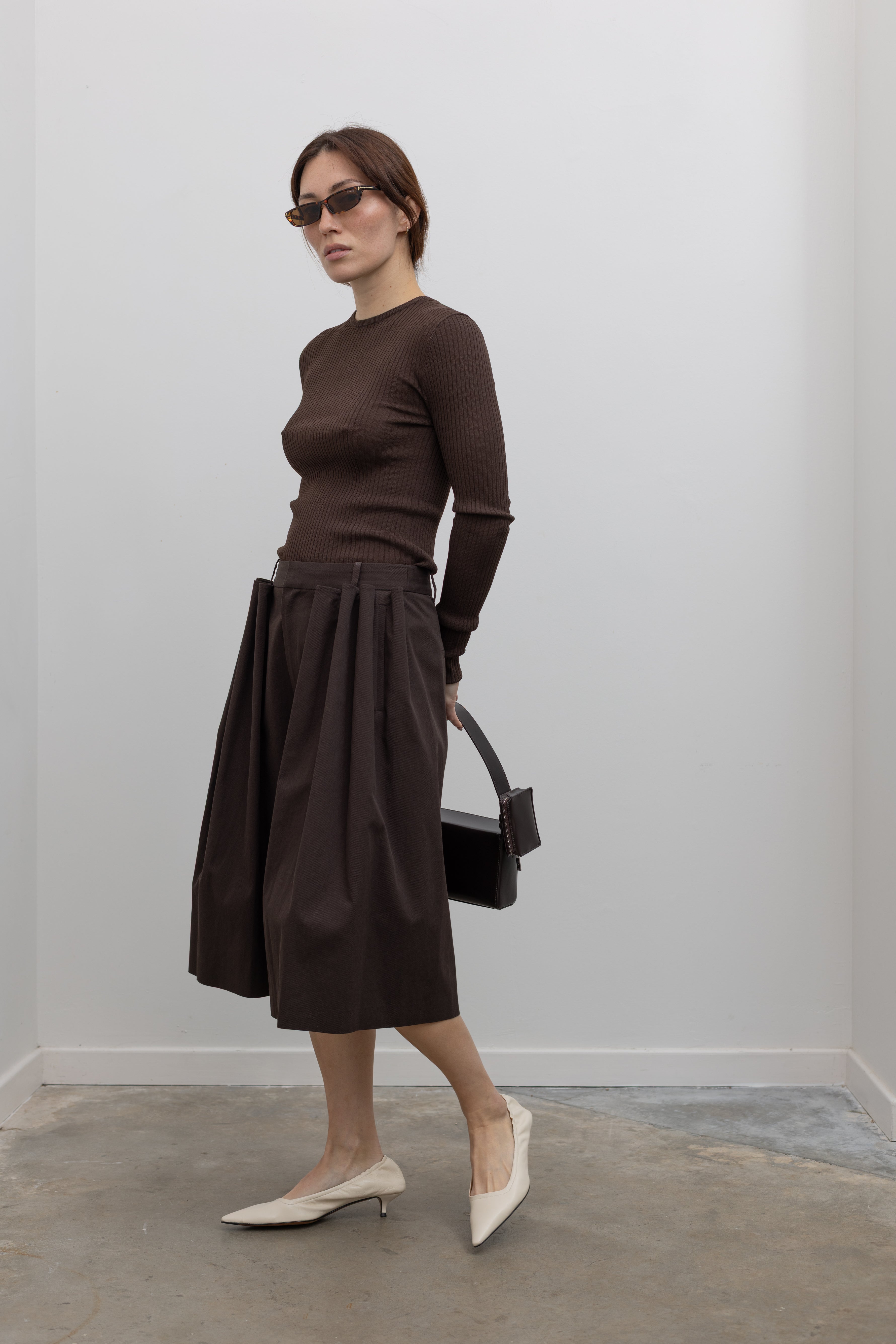 Woman standing wearing Spring fashion in a brown ribbed sweater and Tibi Brown Luxe Spring Twill Tucked Pleated Wide Leg Short at Alas Eius