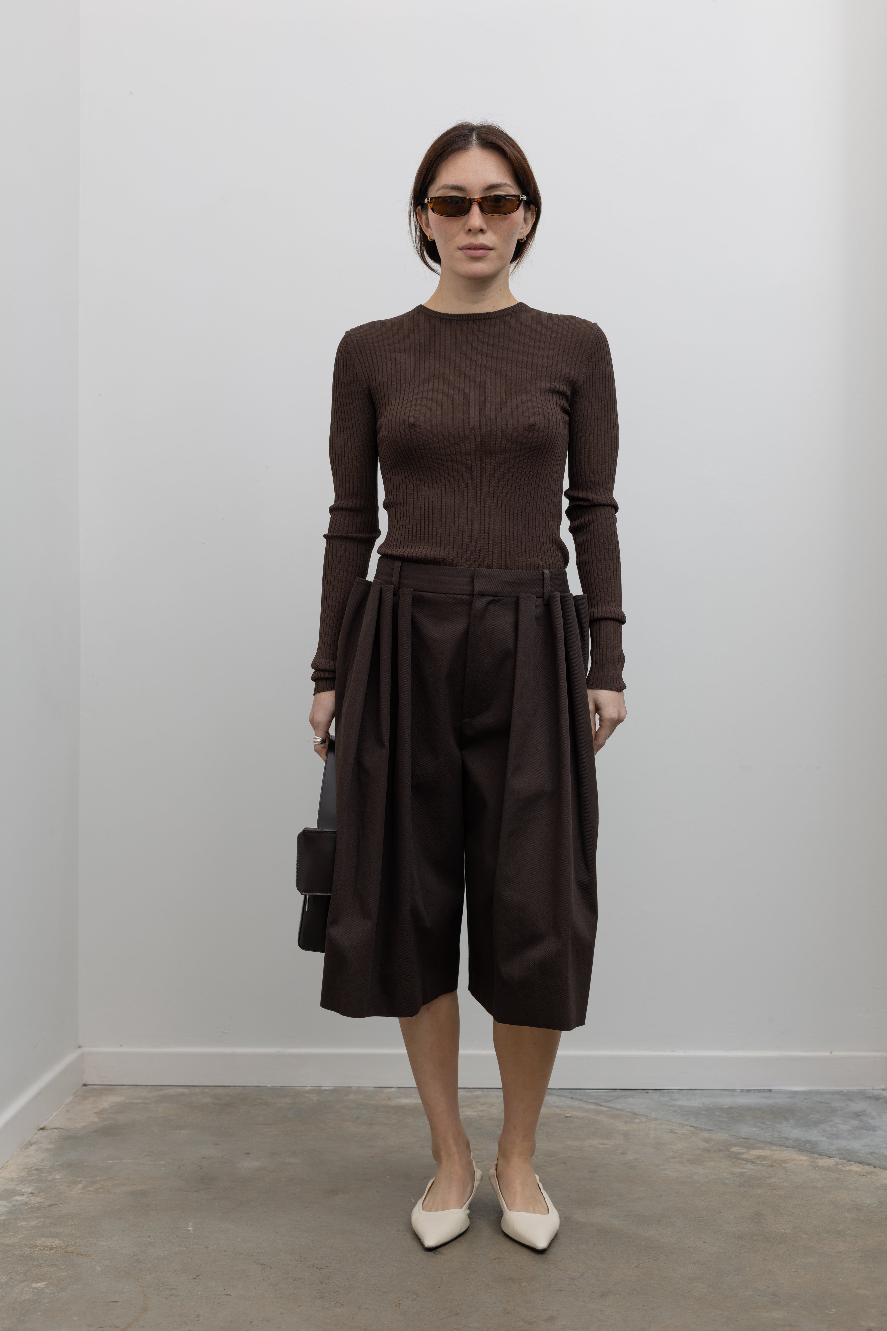 Woman standing wearing Spring fashion in a Tibi Brown Ribbed Sweater Crewneck Pullover with a pair of brown pleated trousers at Alas Eius