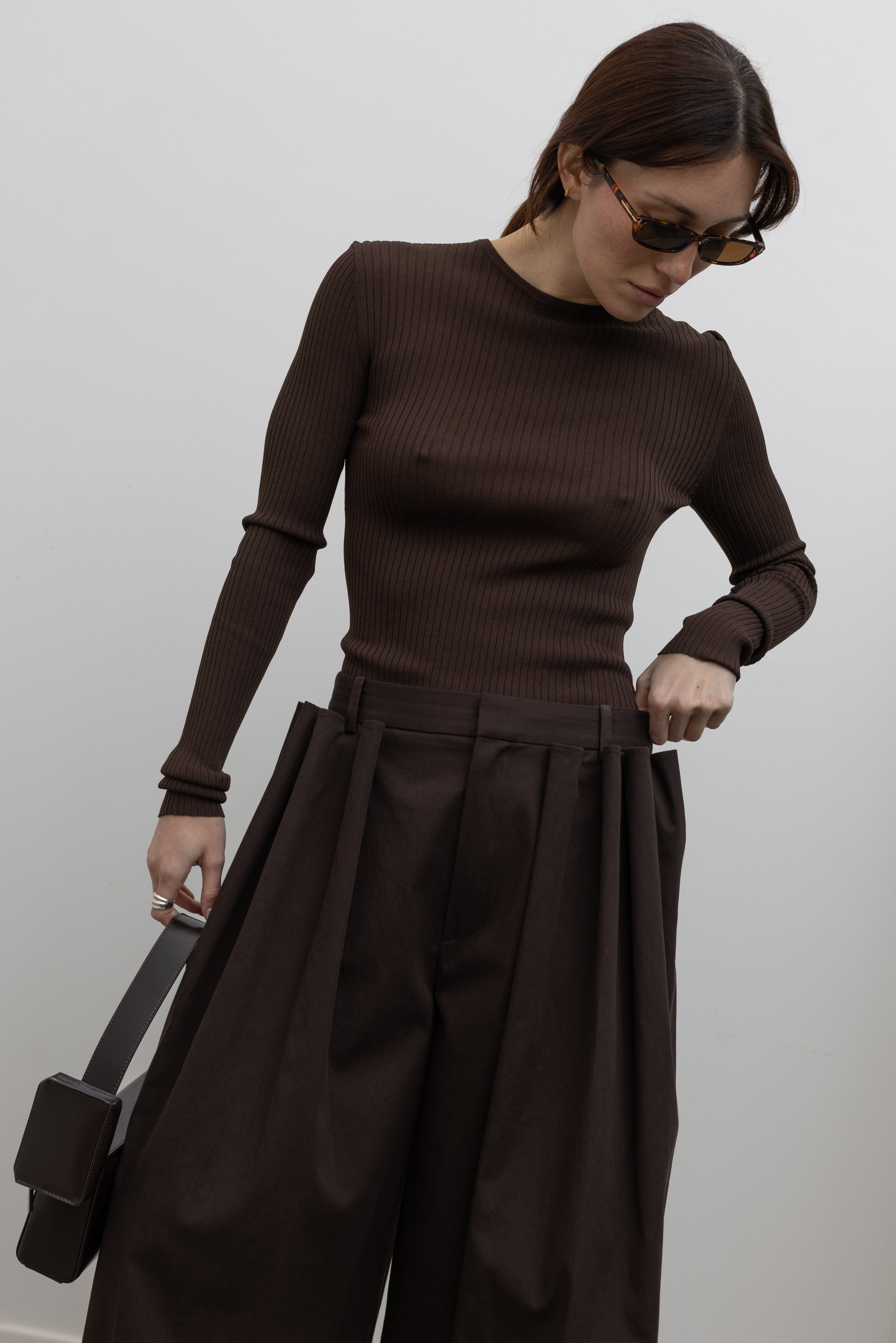 Woman standing wearing Spring fashion in a Tibi Brown Ribbed Sweater Crewneck Pullover with a pair of brown pleated trousers at Alas Eius
