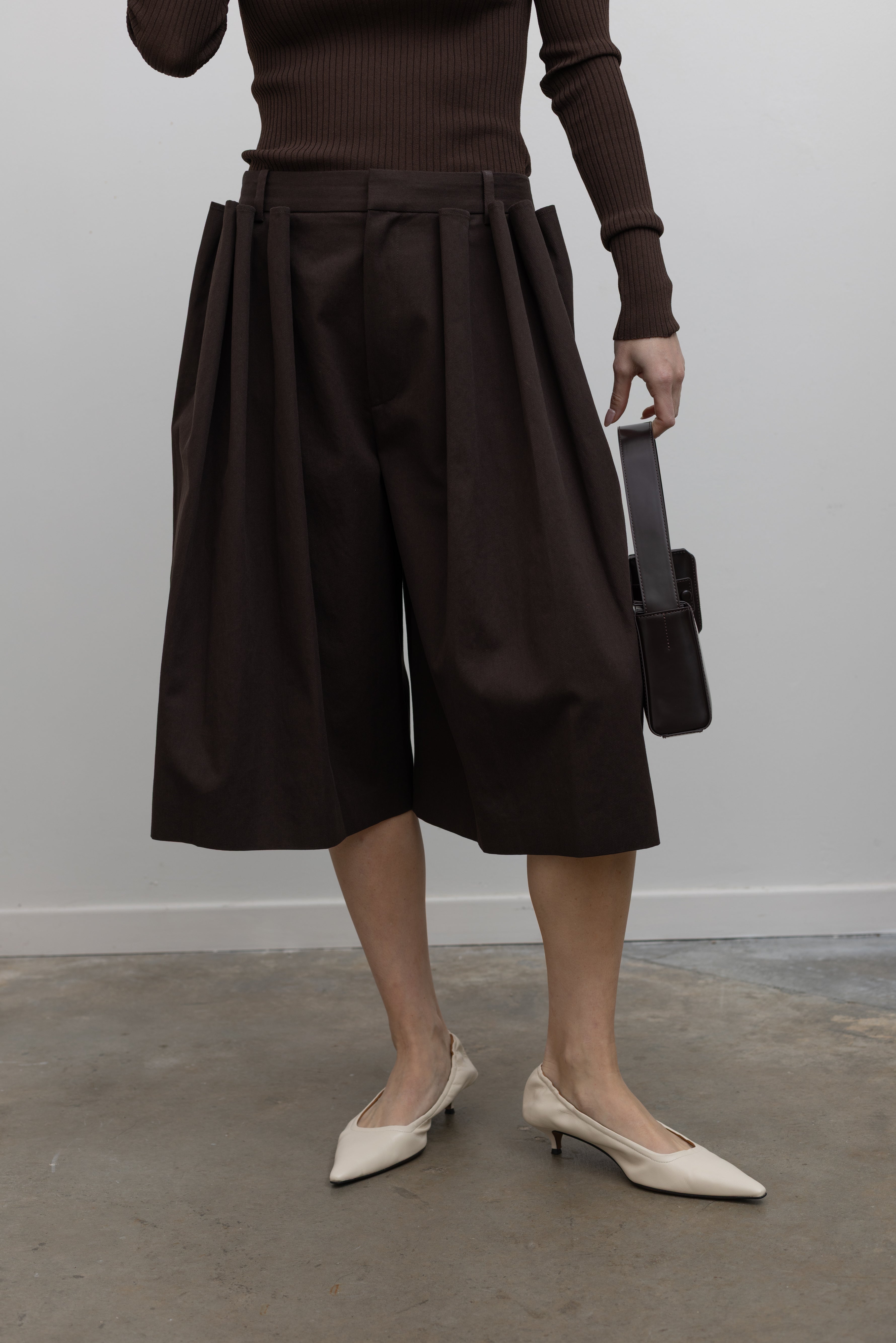 Woman wearing Spring fashion in a brown ribbed sweater and Tibi Brown Luxe Spring Twill Tucked Pleated Wide Leg Short at Alas Eius