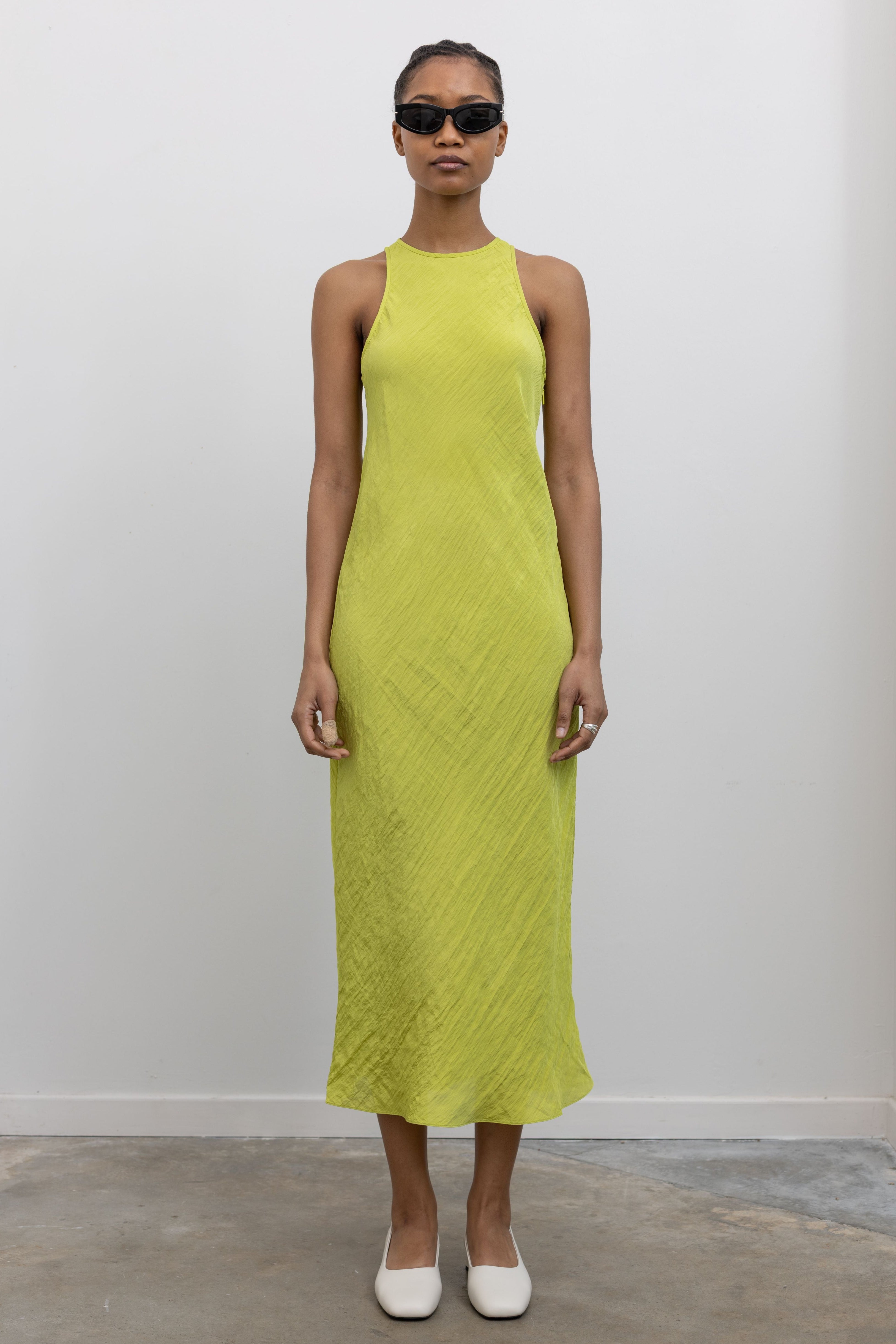 Woman standing wearing Spring fashion in a Tibi Crinkle Slip Midi Bias Dress with sunglasses and white pumps at Alas Eius