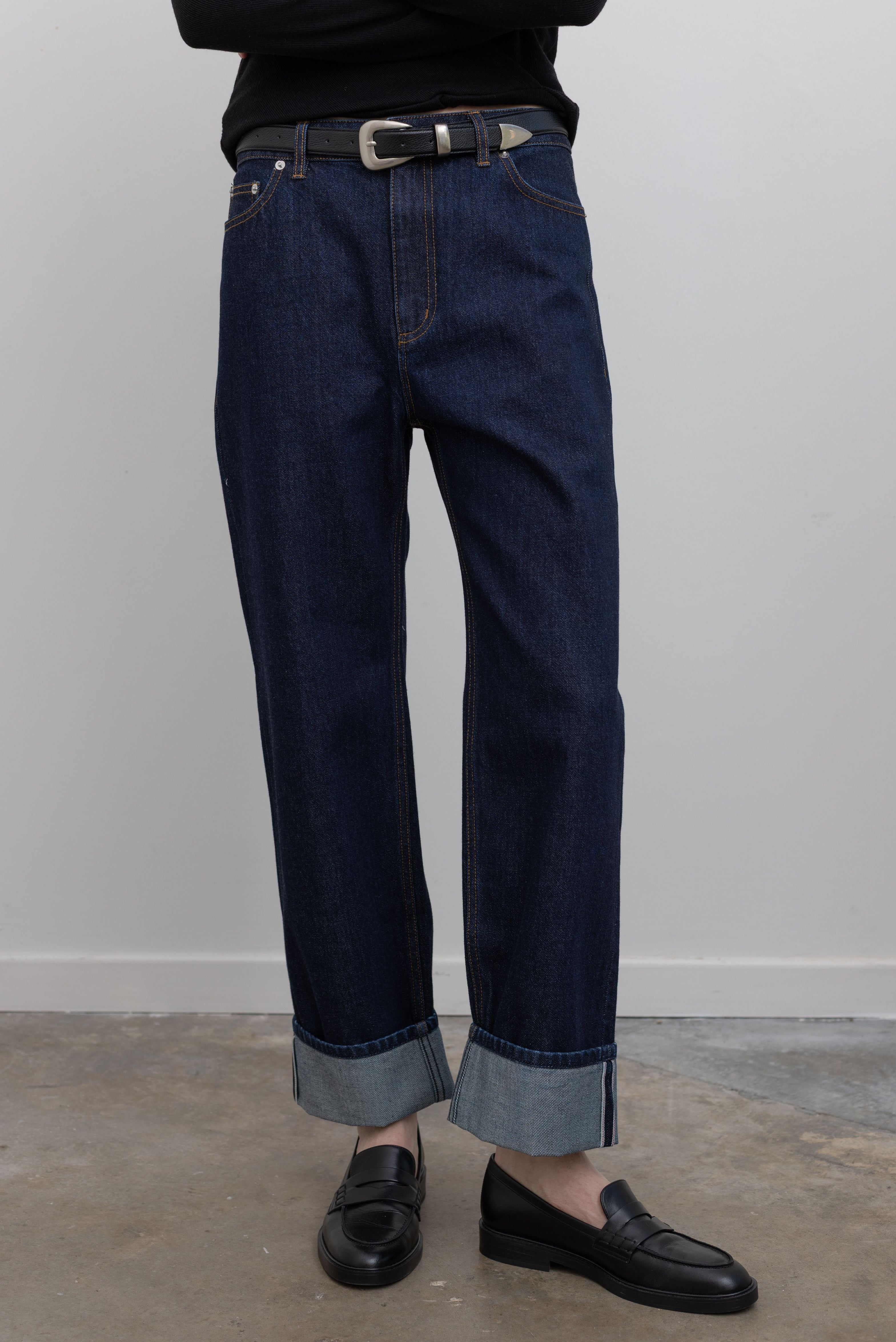 Woman standing wearing Spring fashion in a pair of Tibi Selvedge Denim 5 Pocket Alec Jean with a black leather belt and black leather loafers at Alas Eius