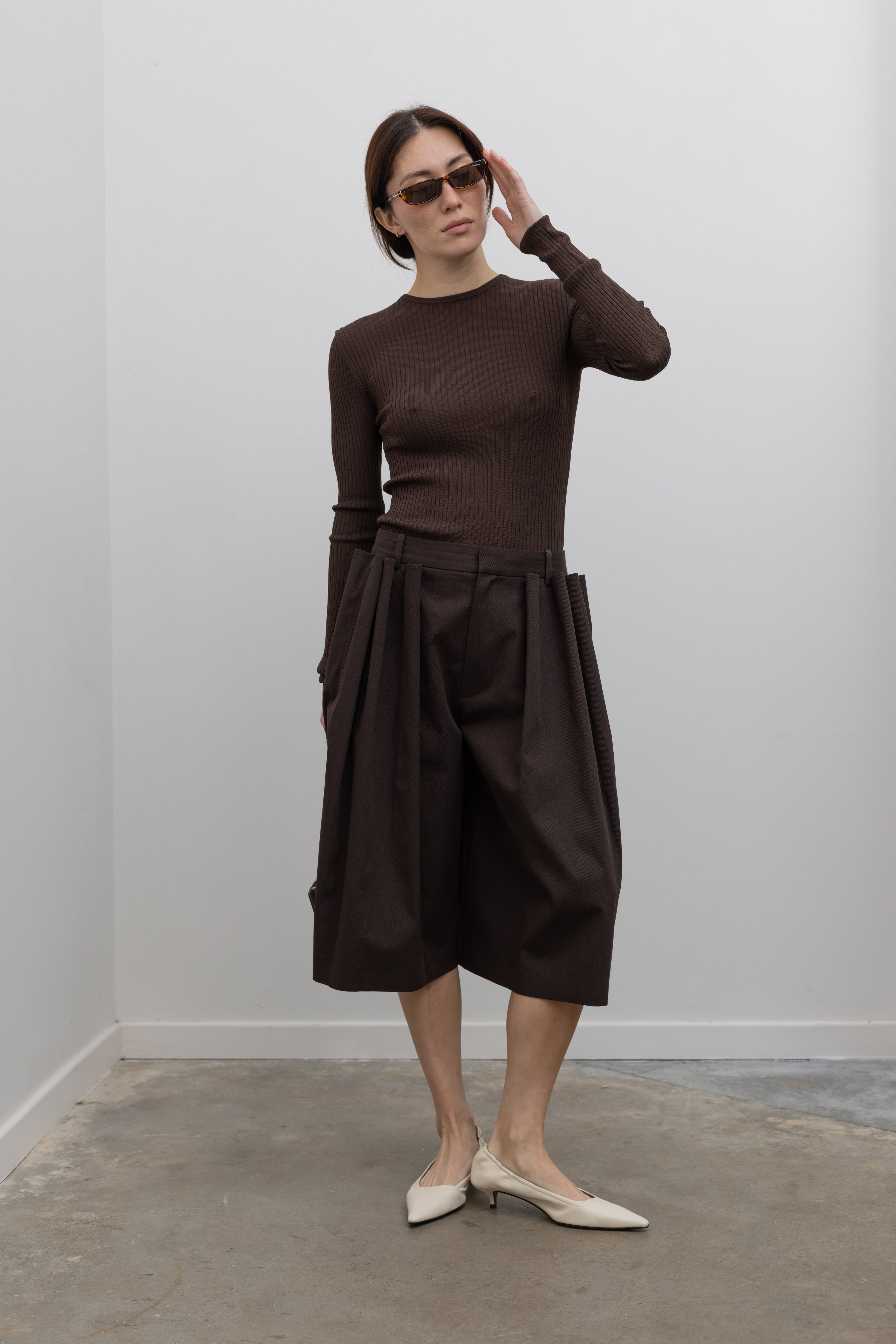 Woman wearing Spring fashion in a brown ribbed sweater and Tibi Brown Luxe Spring Twill Tucked Pleated Wide Leg Short at Alas Eius