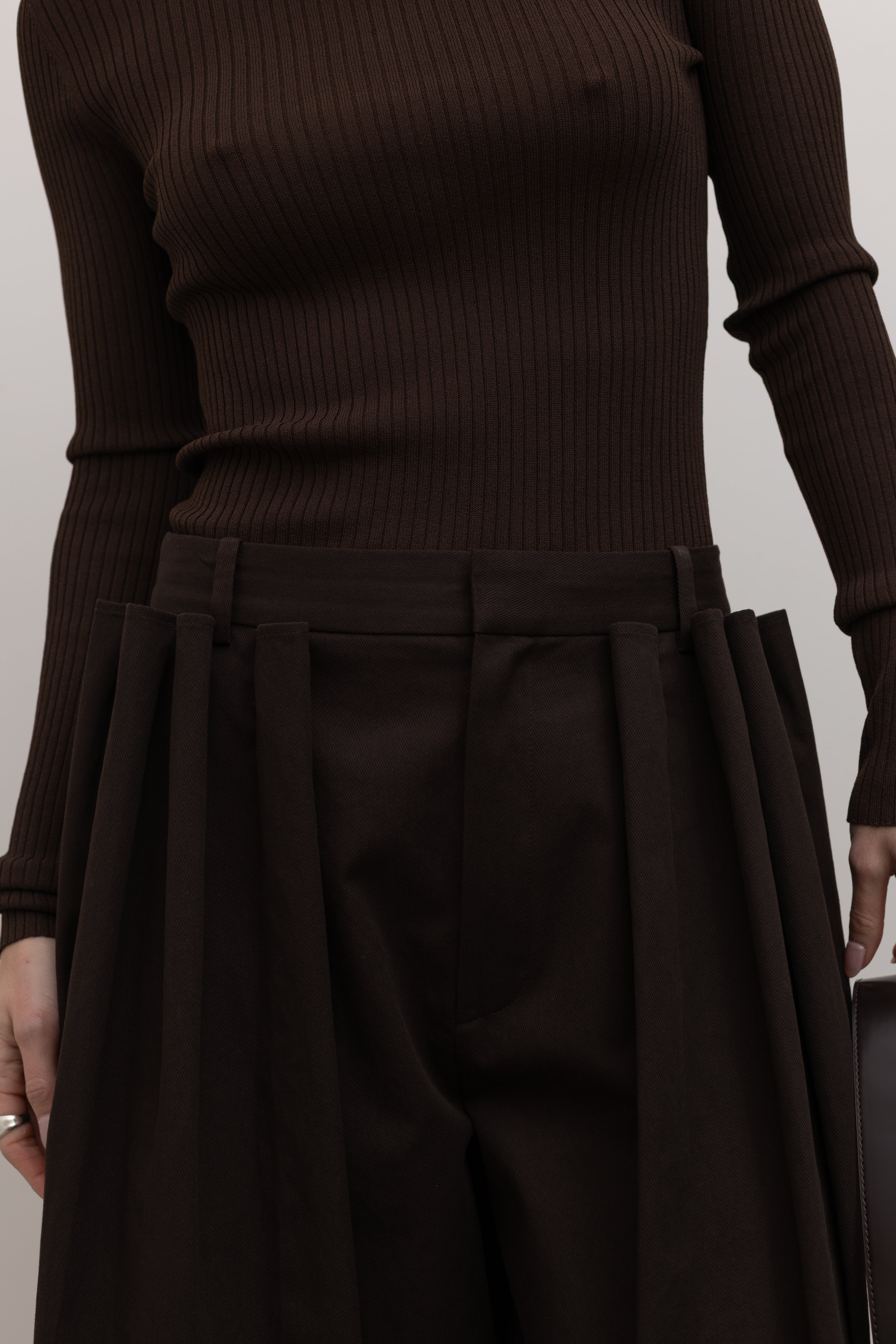 Detailed product view of Woman standing wearing Spring fashion in a Tibi Brown Ribbed Sweater Crewneck Pullover with a pair of brown pleated trousers at Alas Eius