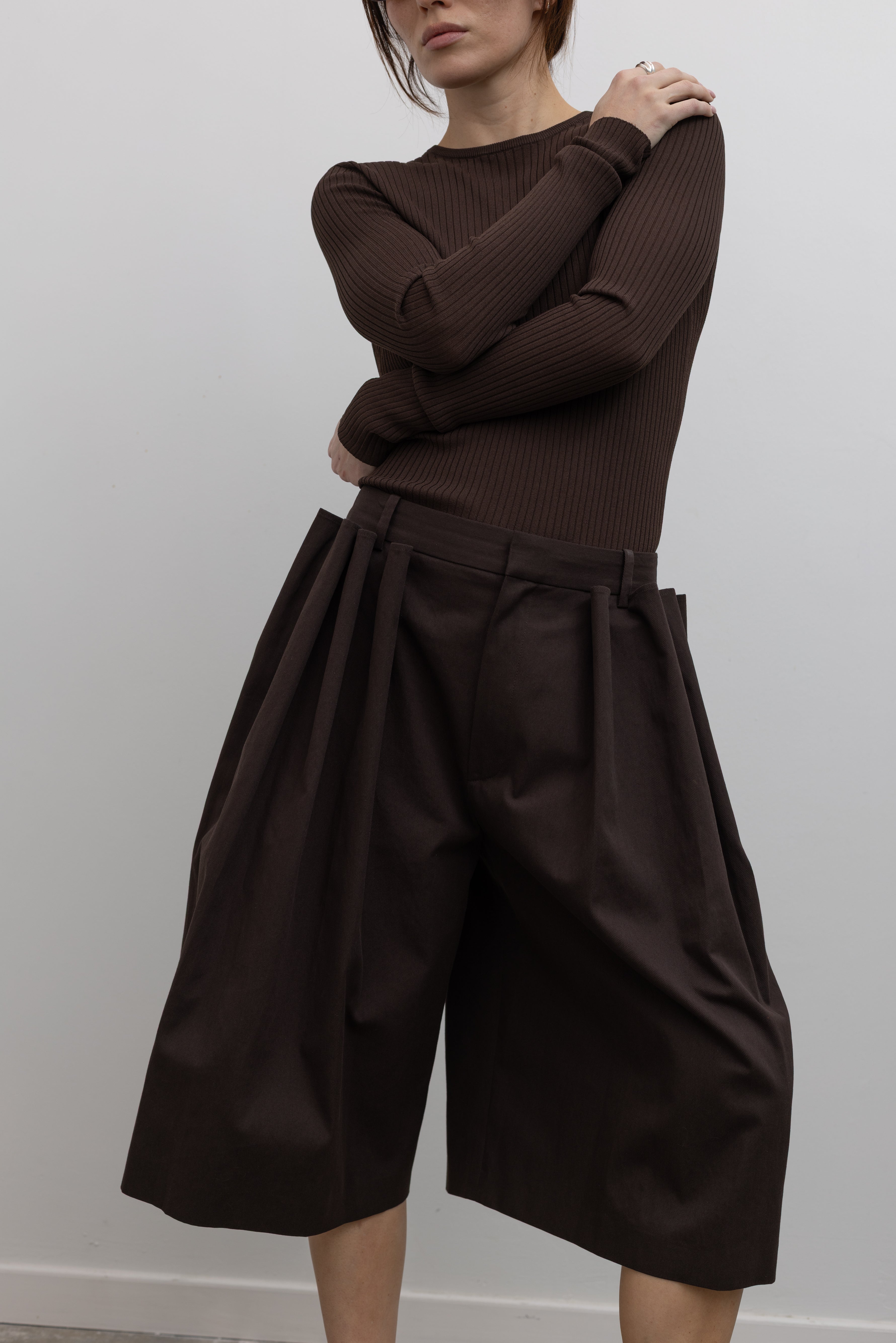 Detailed product view of Woman standing wearing Spring fashion in a Tibi Brown Ribbed Sweater Crewneck Pullover with a pair of brown pleated culottes at Alas Eius