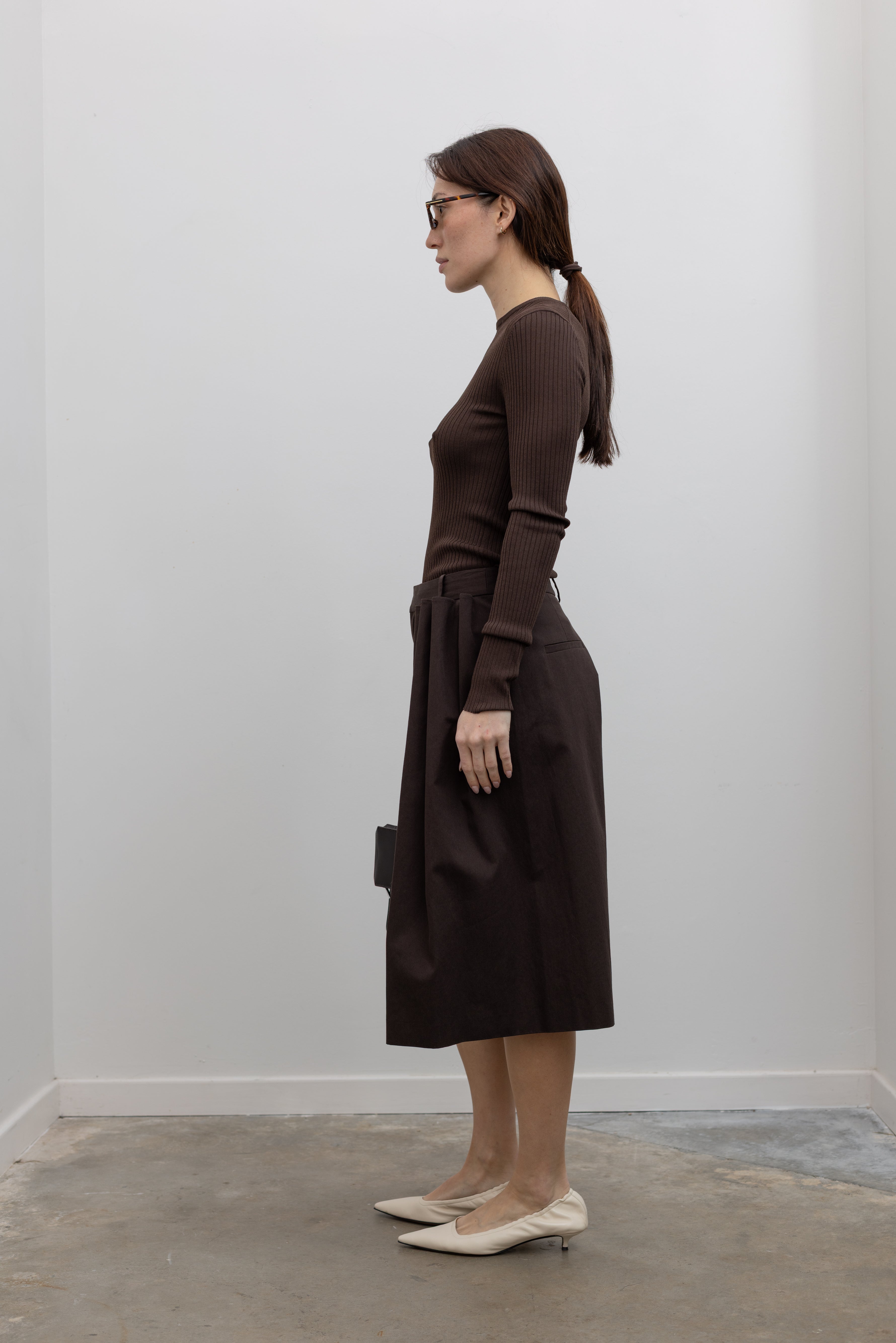 Side view of Woman standing wearing Spring fashion in a Tibi Brown Ribbed Sweater Crewneck Pullover with a pair of brown pleated culottes at Alas Eius