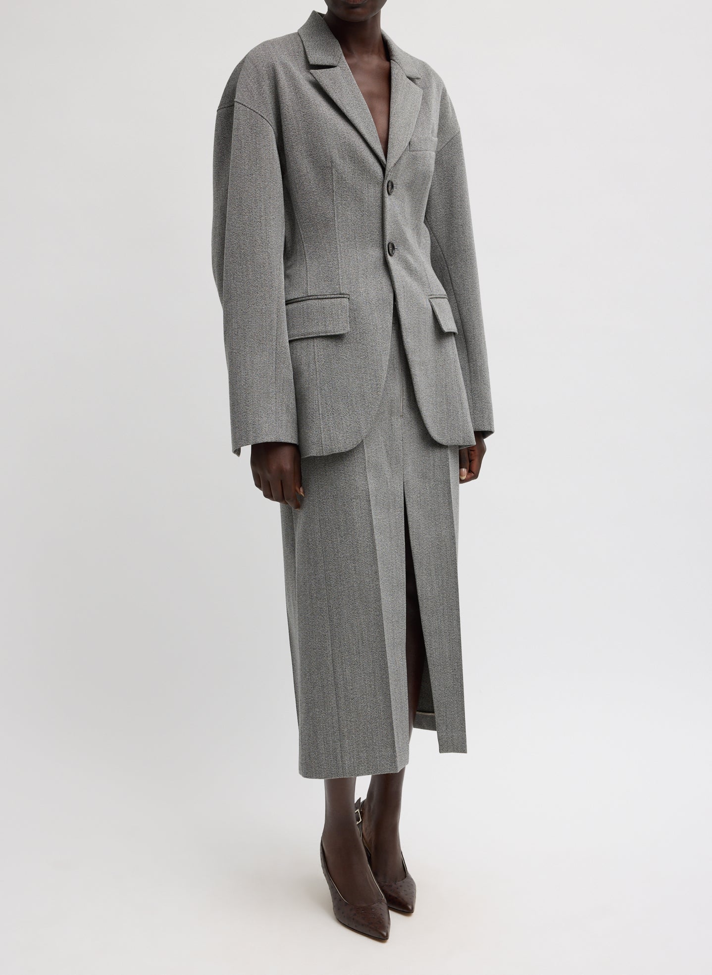 Woman standing wearing chic and modern spring fashion in the Tibi Structured Wool Sculpted Blazer crafted from firm, refined virgin wool and features a blousant back with sculpted seaming and a button-front closure at an Alas Eius store. 