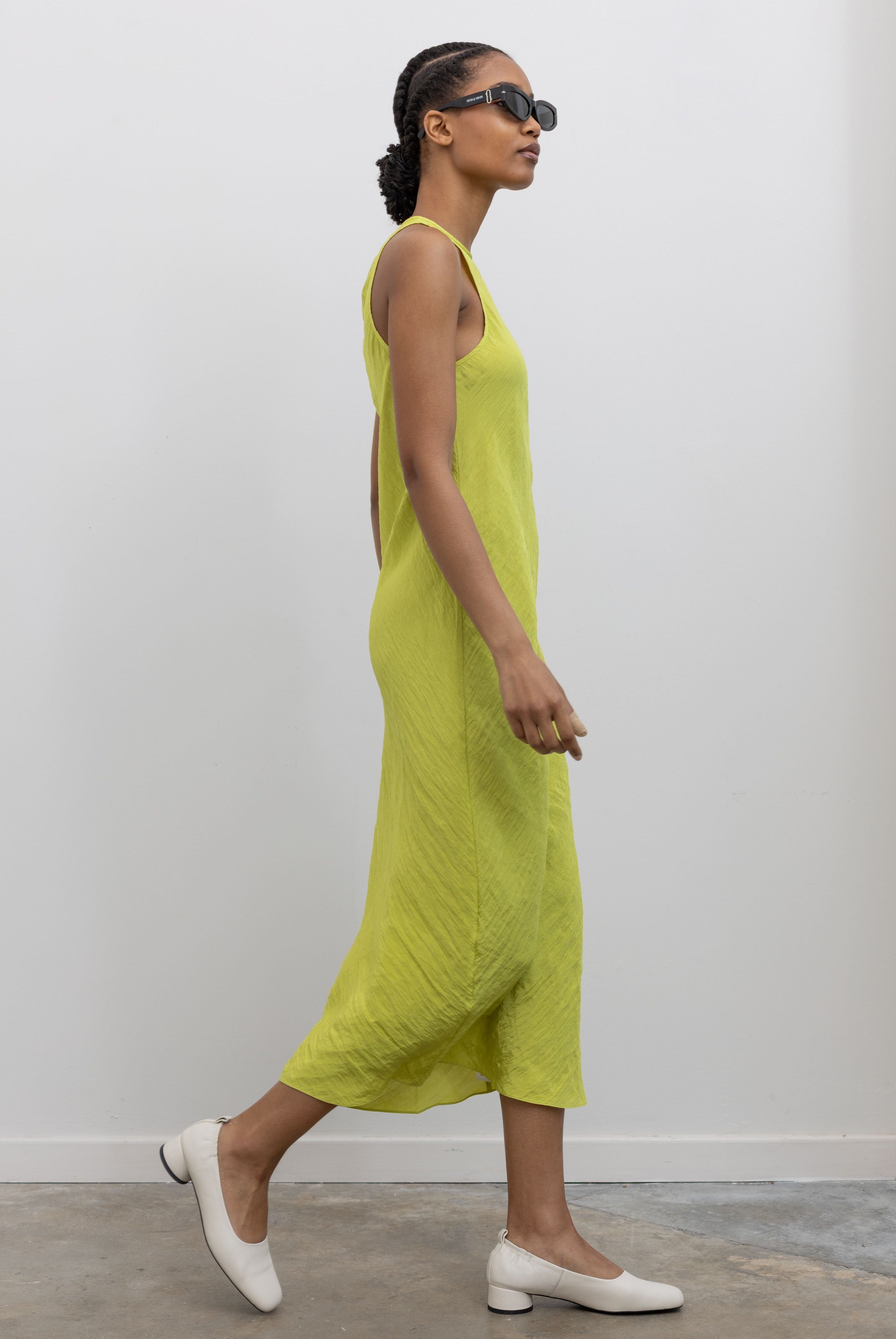 Side view of Woman walking wearing Spring fashion in a Tibi Crinkle Slip Midi Bias Dress with sunglasses and white pumps at Alas Eius