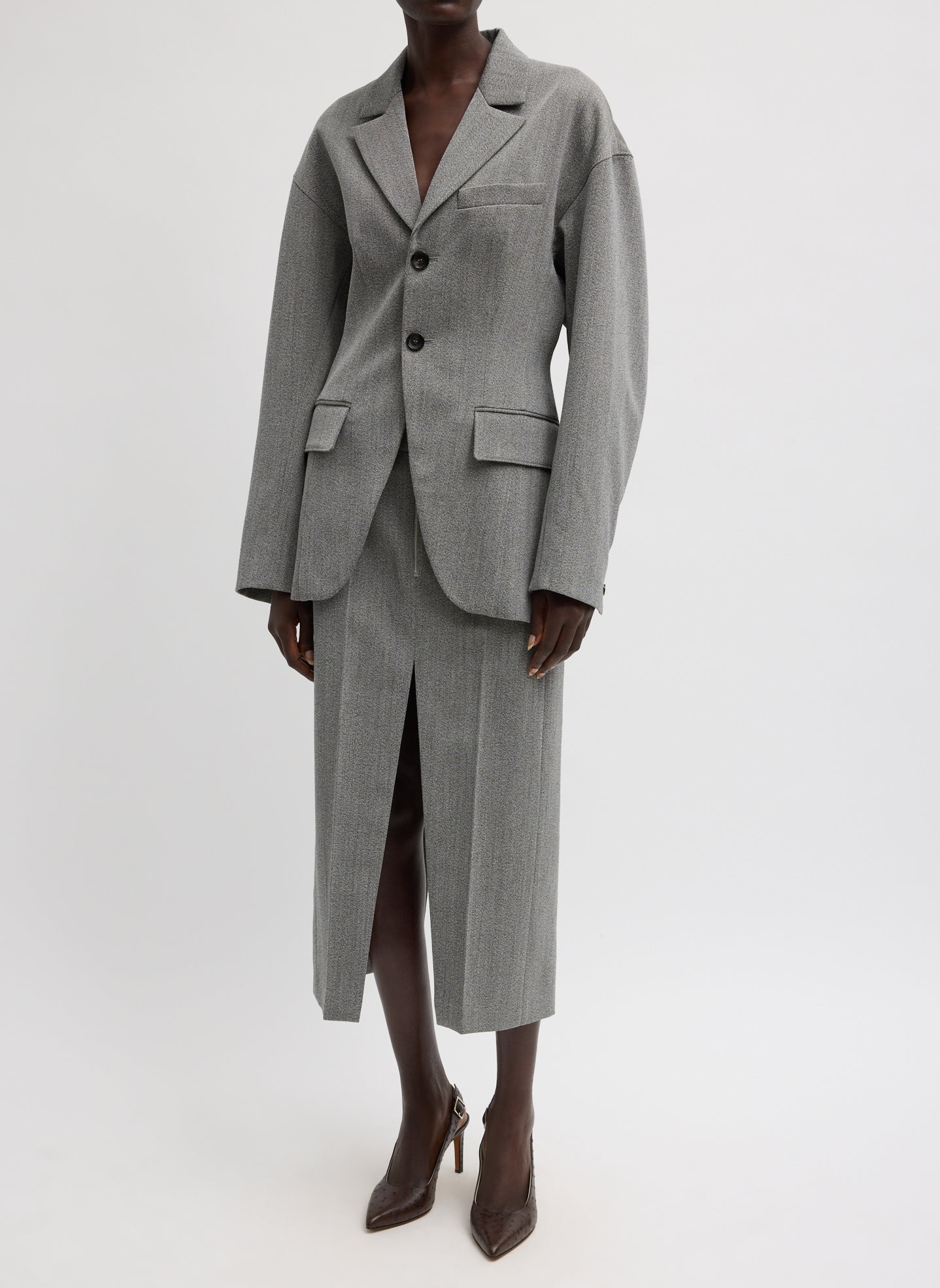 Woman standing wearing chic and modern spring fashion in the Tibi Structured Wool Sculpted Blazer crafted from firm, refined virgin wool and features a blousant back with sculpted seaming and a button-front closure at an Alas Eius store. 