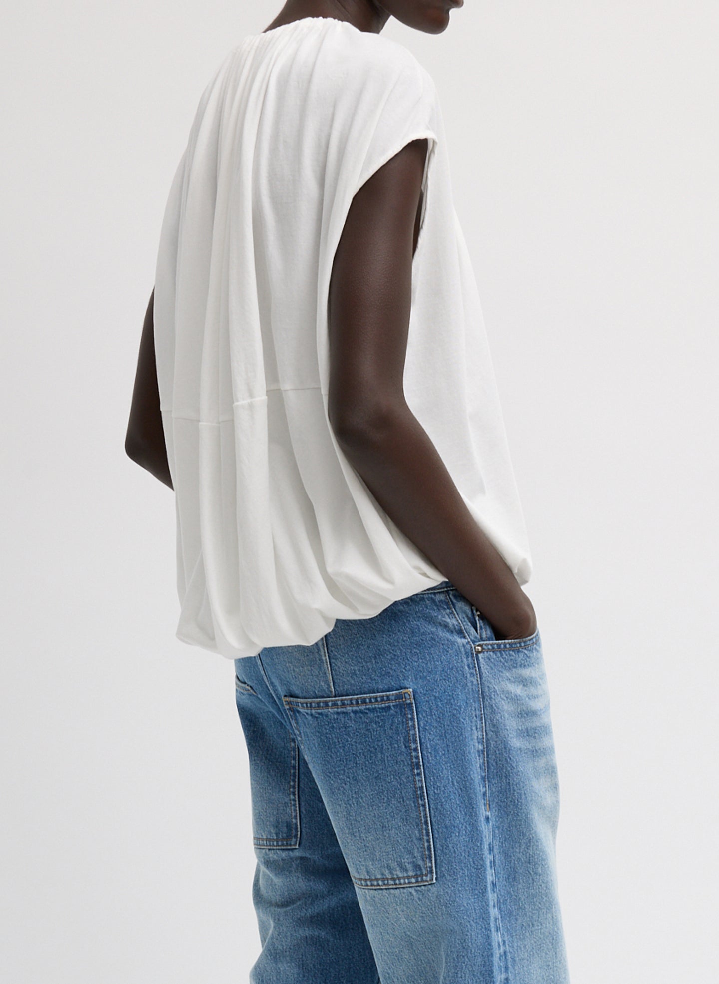 Side view of woman wearing Spring fashion in a pair of light wash jeans and a Tibi White Shirred Neck Circular Cotton T-Shirt at Alas Eius